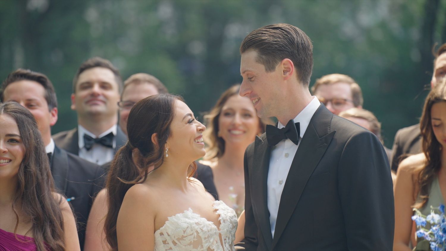 Bride and groom laughing joyfully surrounded by wedding guests during outdoor ceremony celebration.