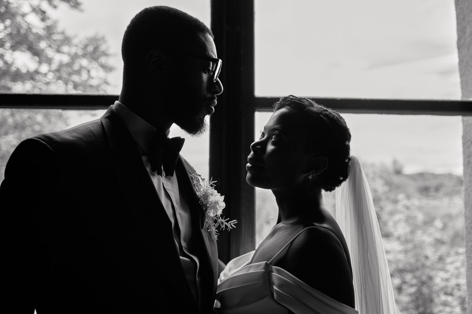 Elegant black and white silhouette portrait of a bride and groom near a bright window.