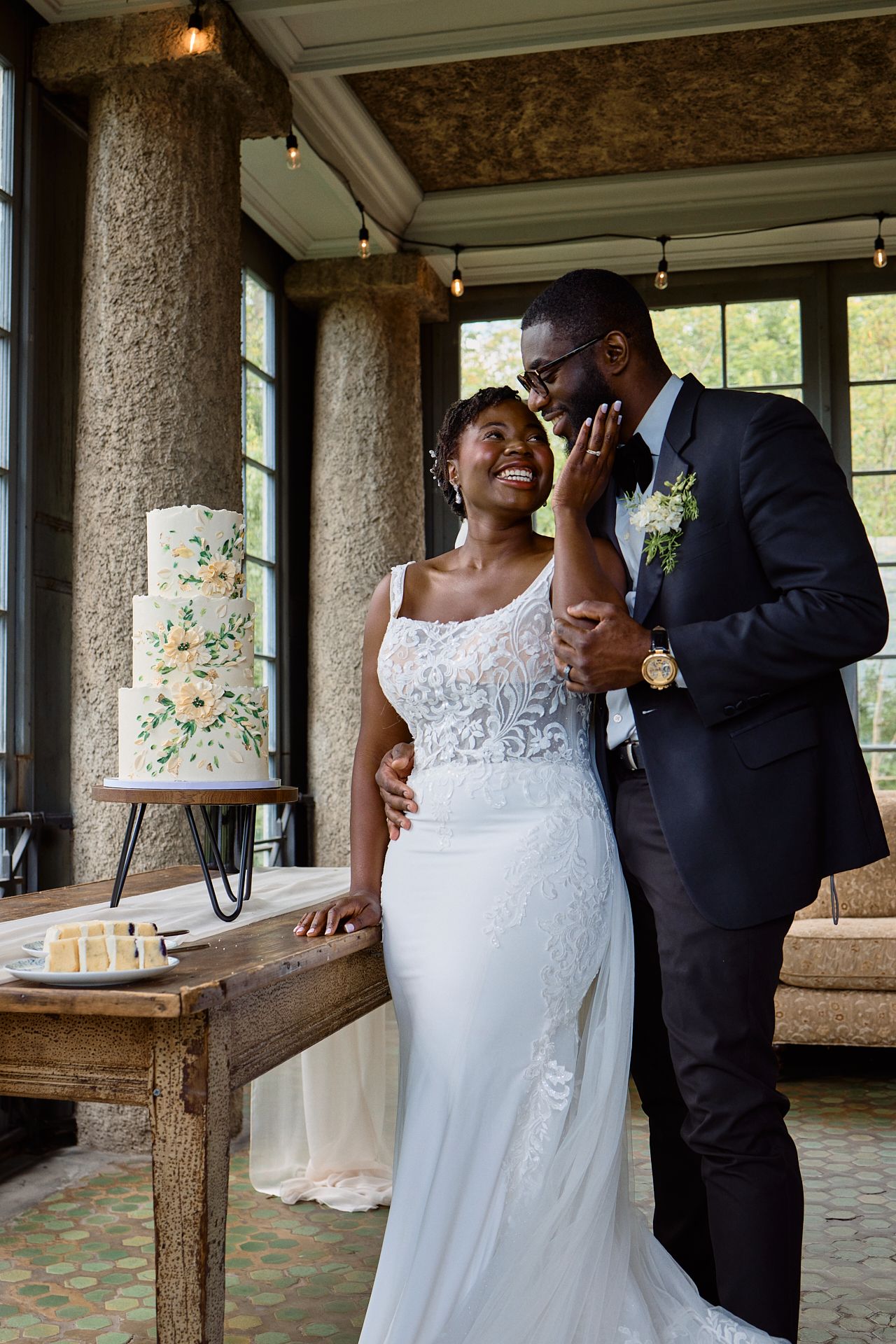 Black couple sharing a romantic moment beside a floral wedding cake in an elegant venue.