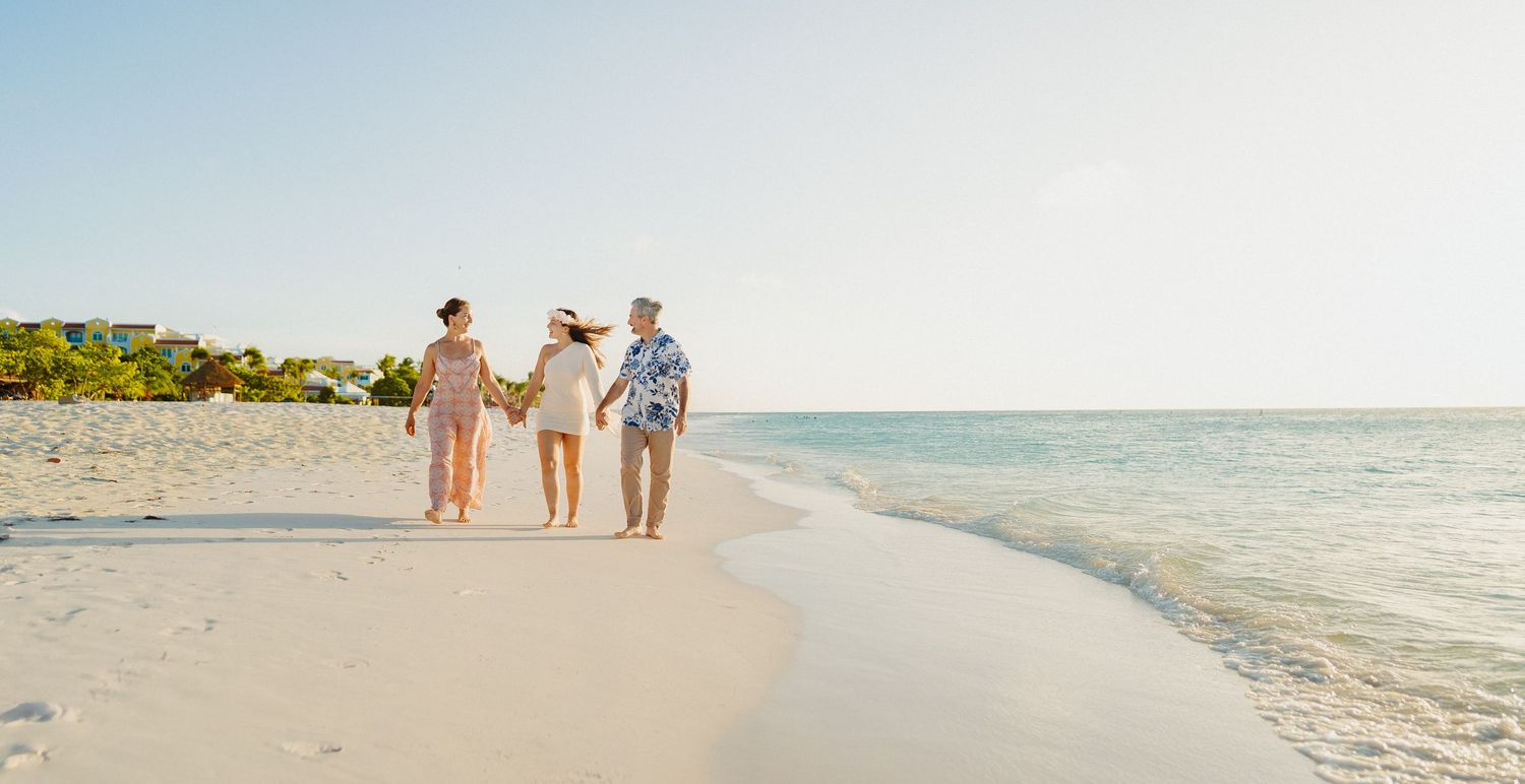 People walking together along a pristine white sand beach with turquoise ocean waters and clear blue sky.