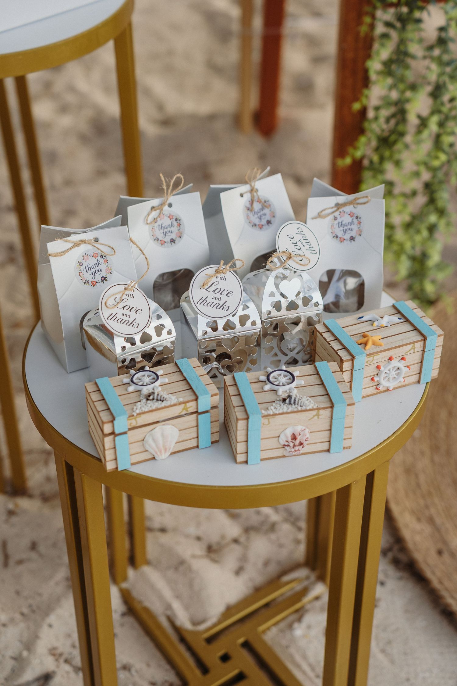 Small decorative gift boxes and favor bags in white and blue colors arranged on a gold side table for a party or celebration.