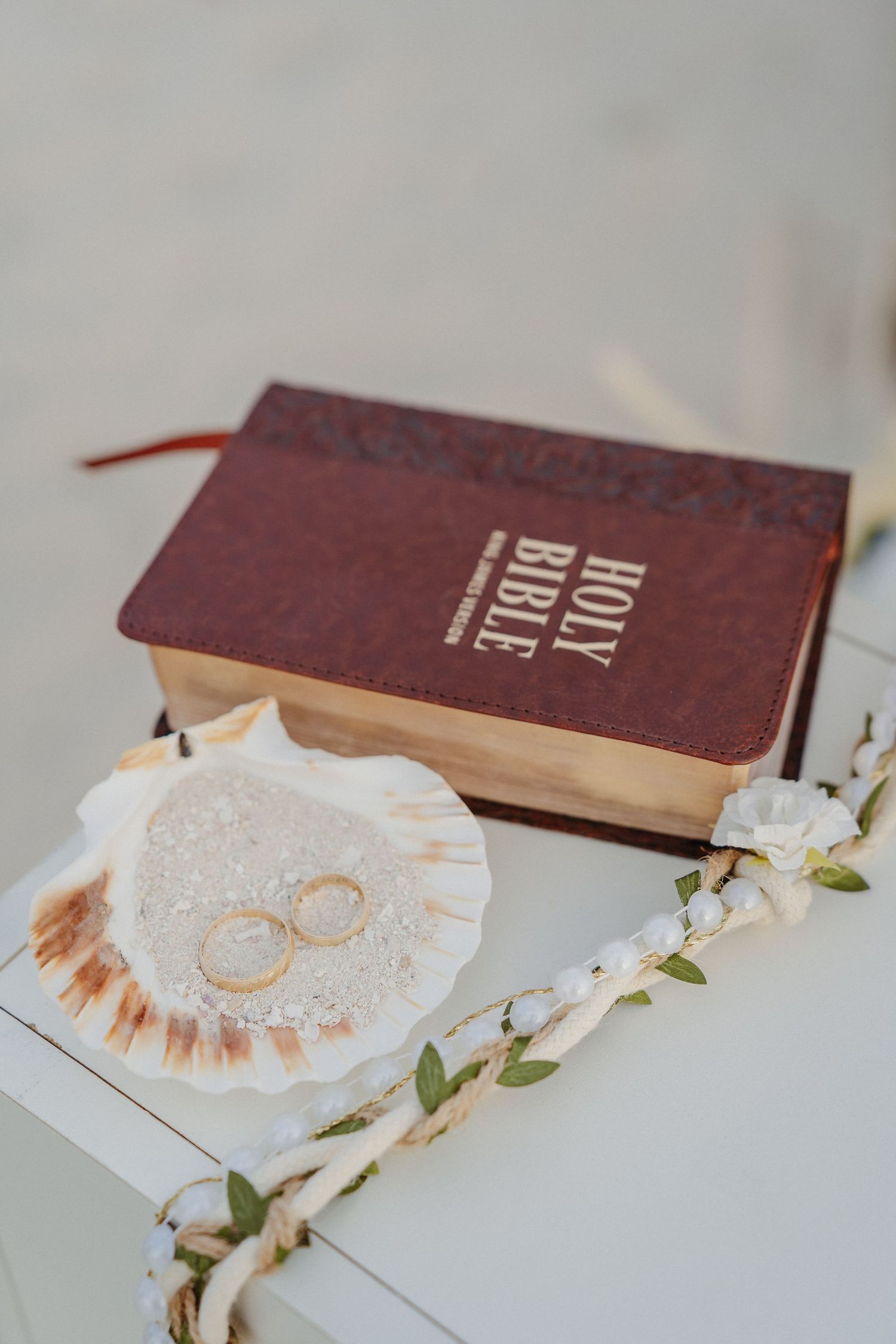 Wedding rings resting on white lace fabric next to a vintage brown book with delicate floral accents.