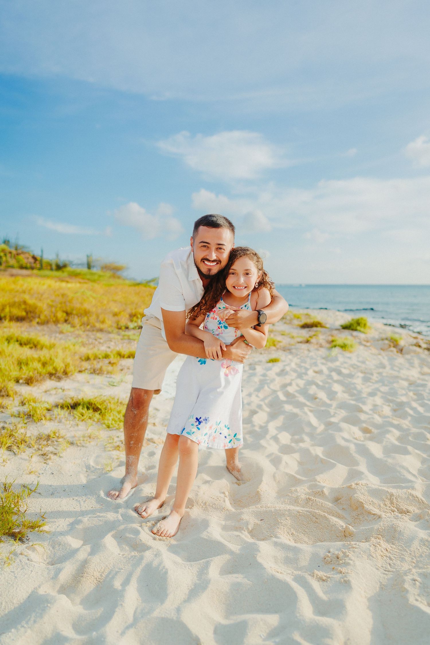 A joyful moment shared between parent and child on a sunny beach with clear blue skies and sandy shores.