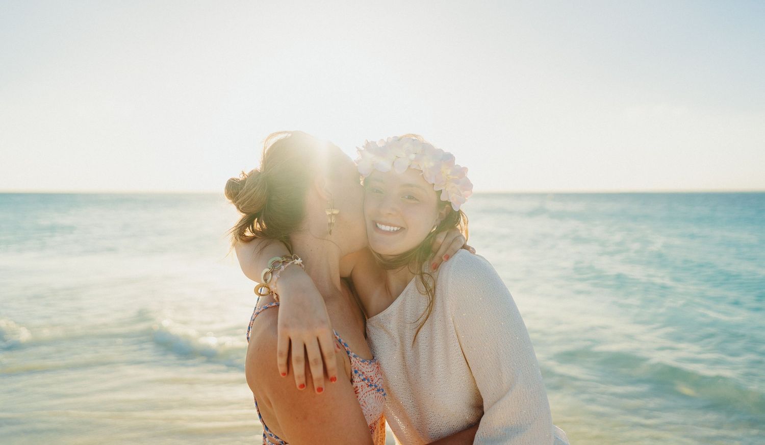 A romantic couple embraces on a sandy beach at sunset with ocean waves in the background.