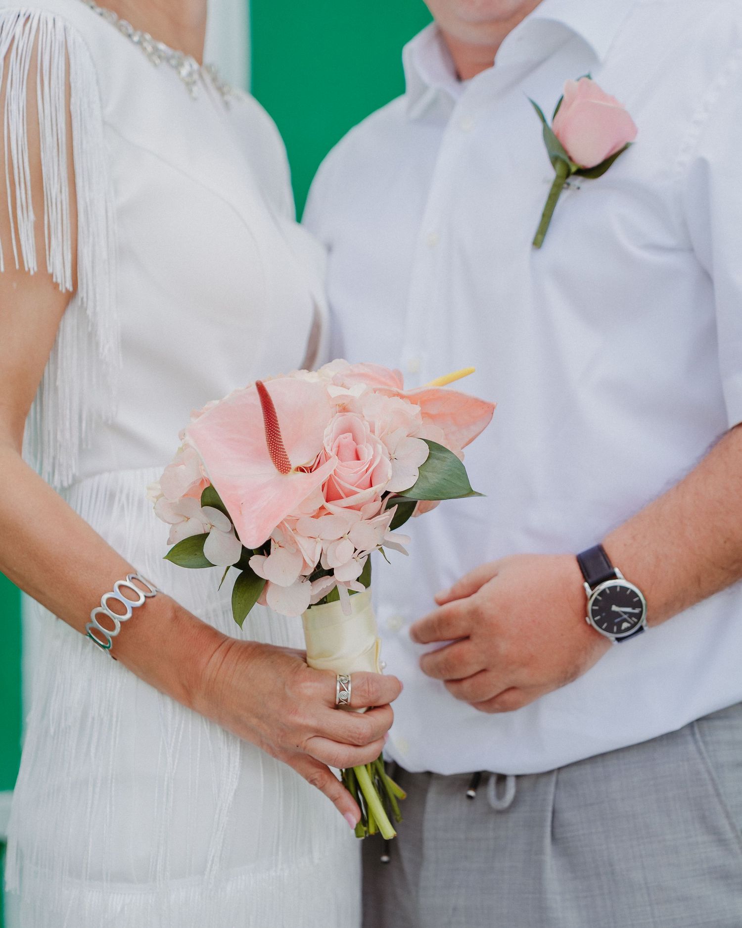 Wedding party members in white attire hold delicate pink bouquets against a green background.