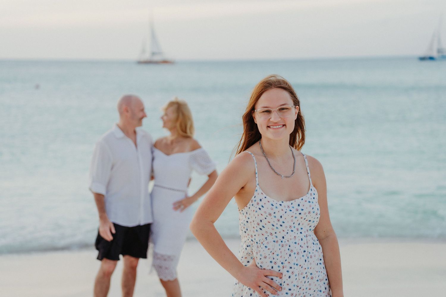 Group walking along a white sandy beach with sailboats visible in the turquoise ocean background.