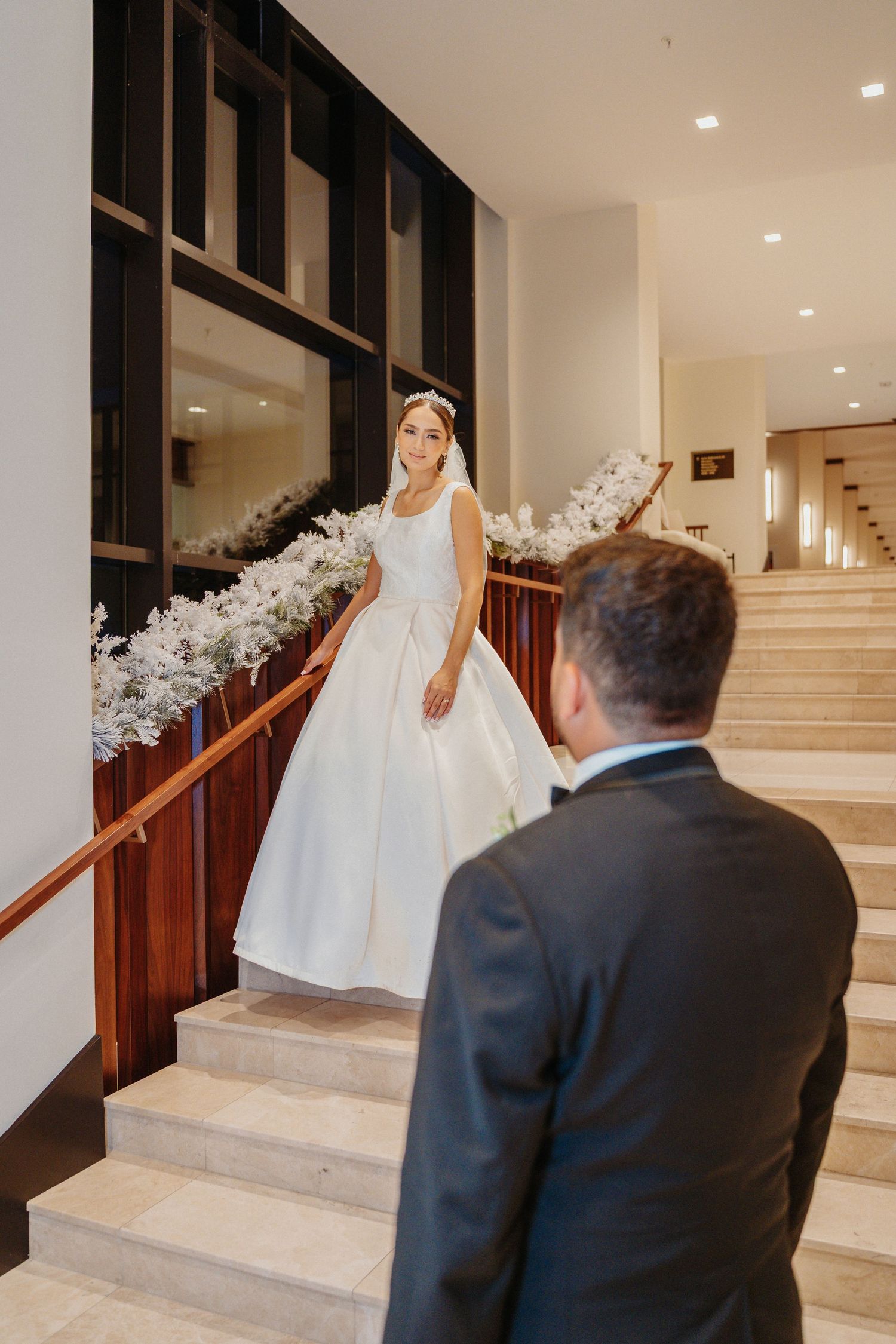 A series of photos showing a bride in a flowing white gown descending an elegant staircase adorned with white floral decor.