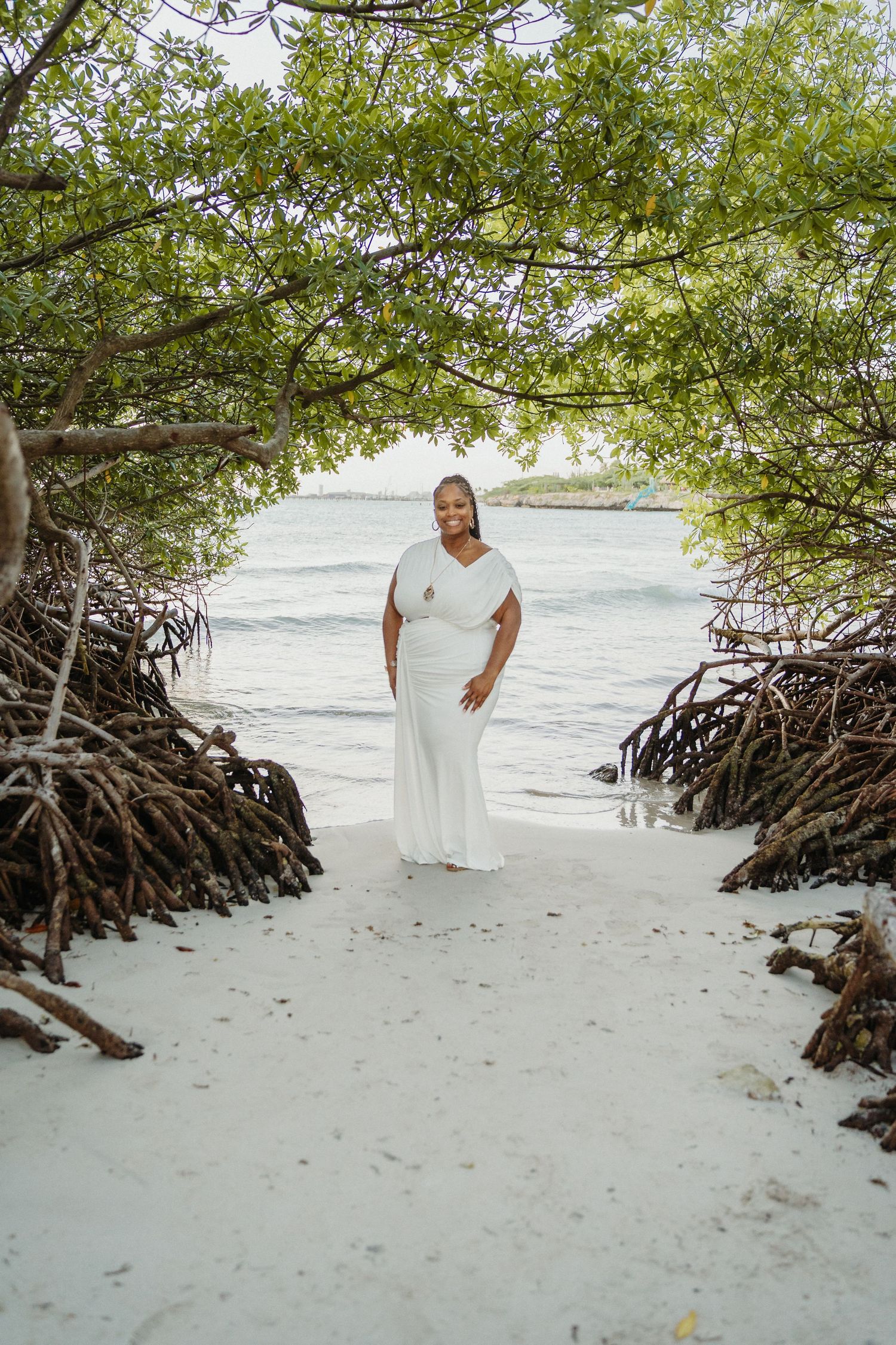 A series of photos capturing someone in a flowing white dress walking and posing on a sandy beach near mangroves.