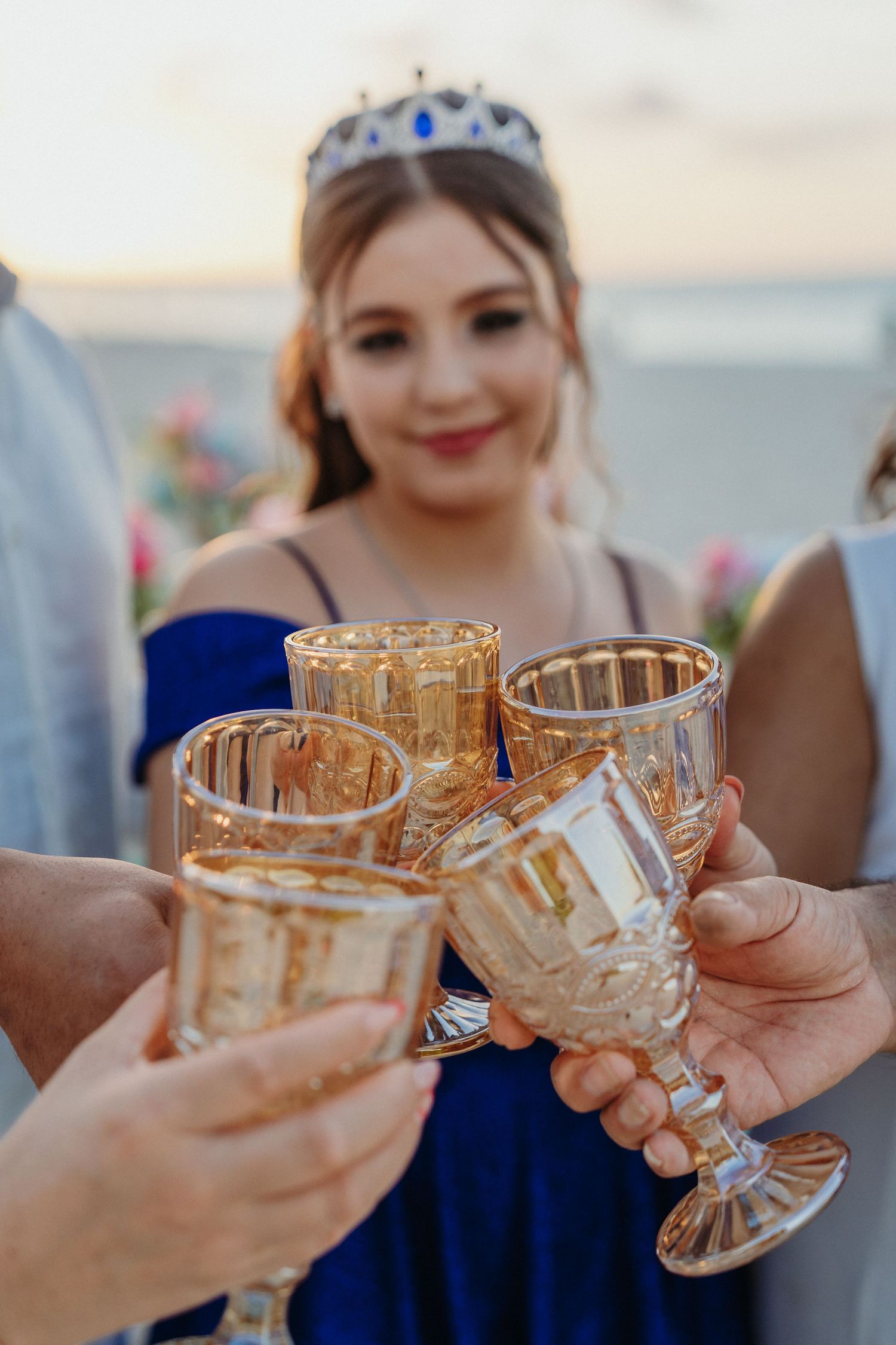 Crystal glasses clink together in a celebratory toast against a beachside sunset backdrop.