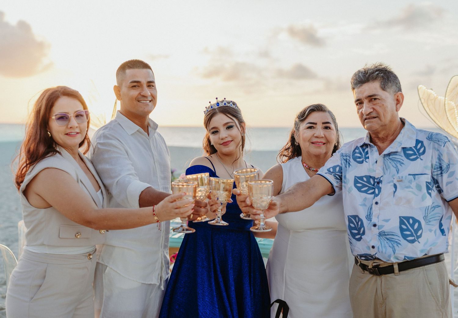 Multi-generational family poses together in coordinated white and blue outfits on a beach at sunset.