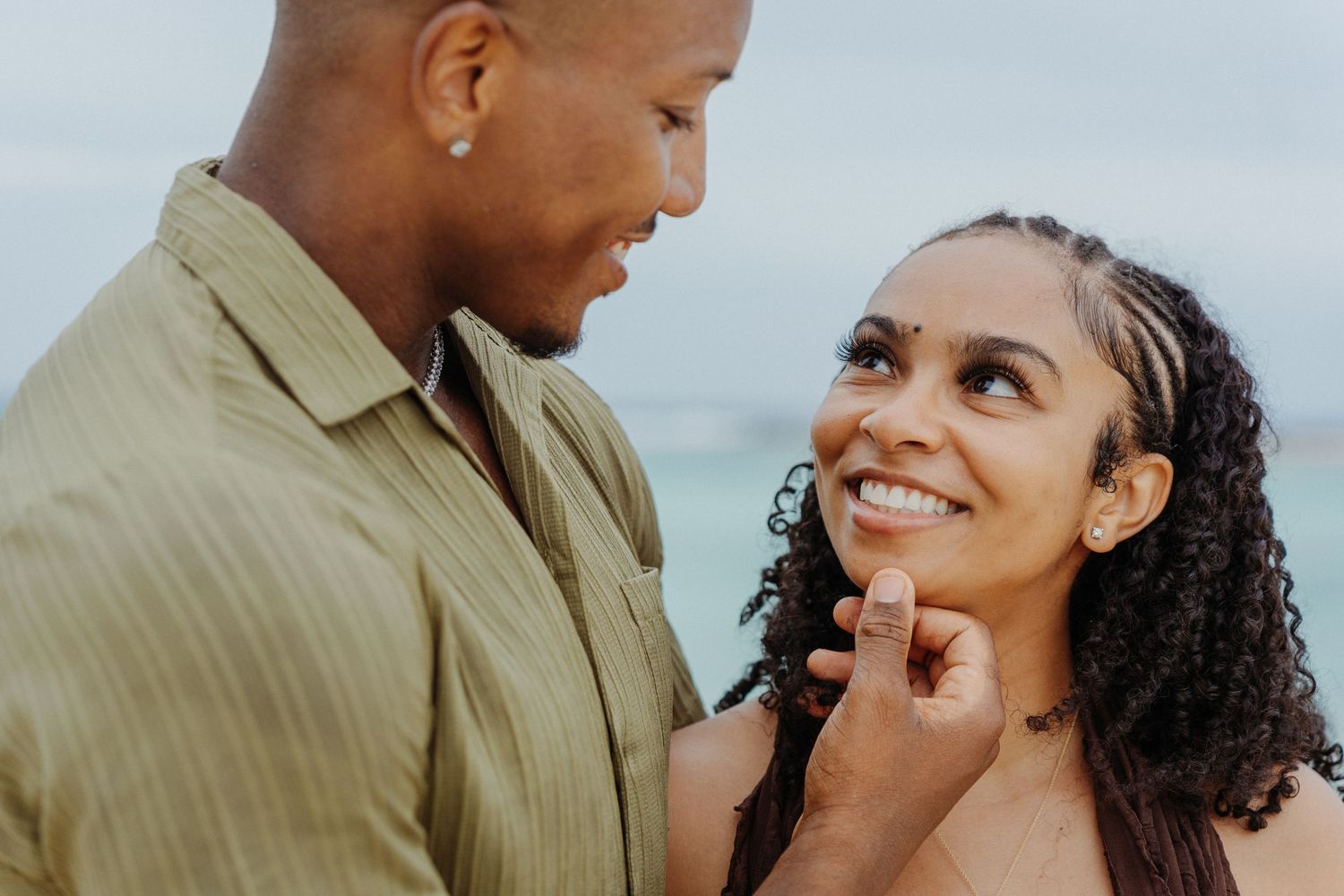 A smiling Black couple shares a tender moment outdoors, man gently touching woman's chin as she gazes up at him.