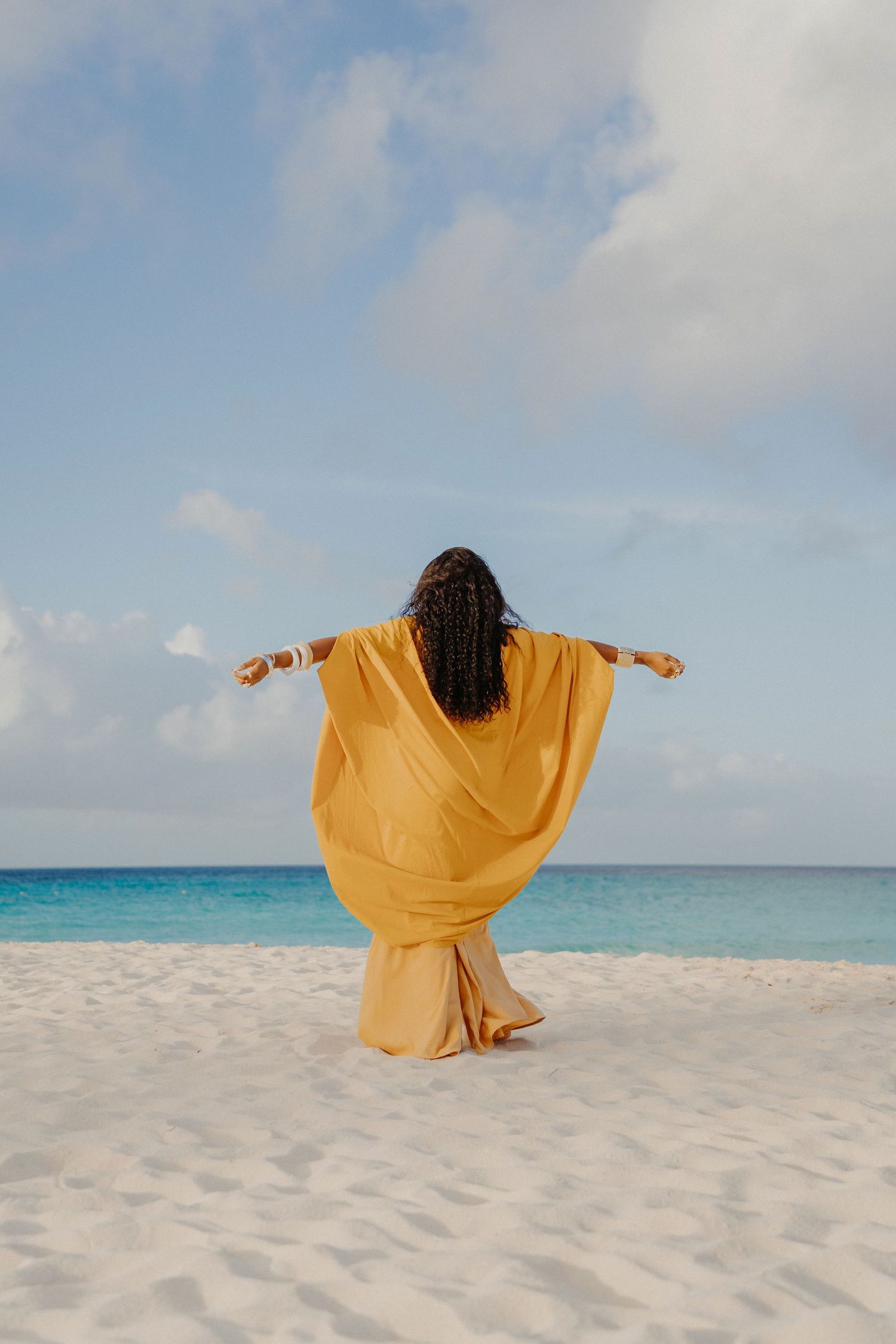 A sequence showing a person in bright yellow attire moving gracefully across white sand with turquoise ocean views.