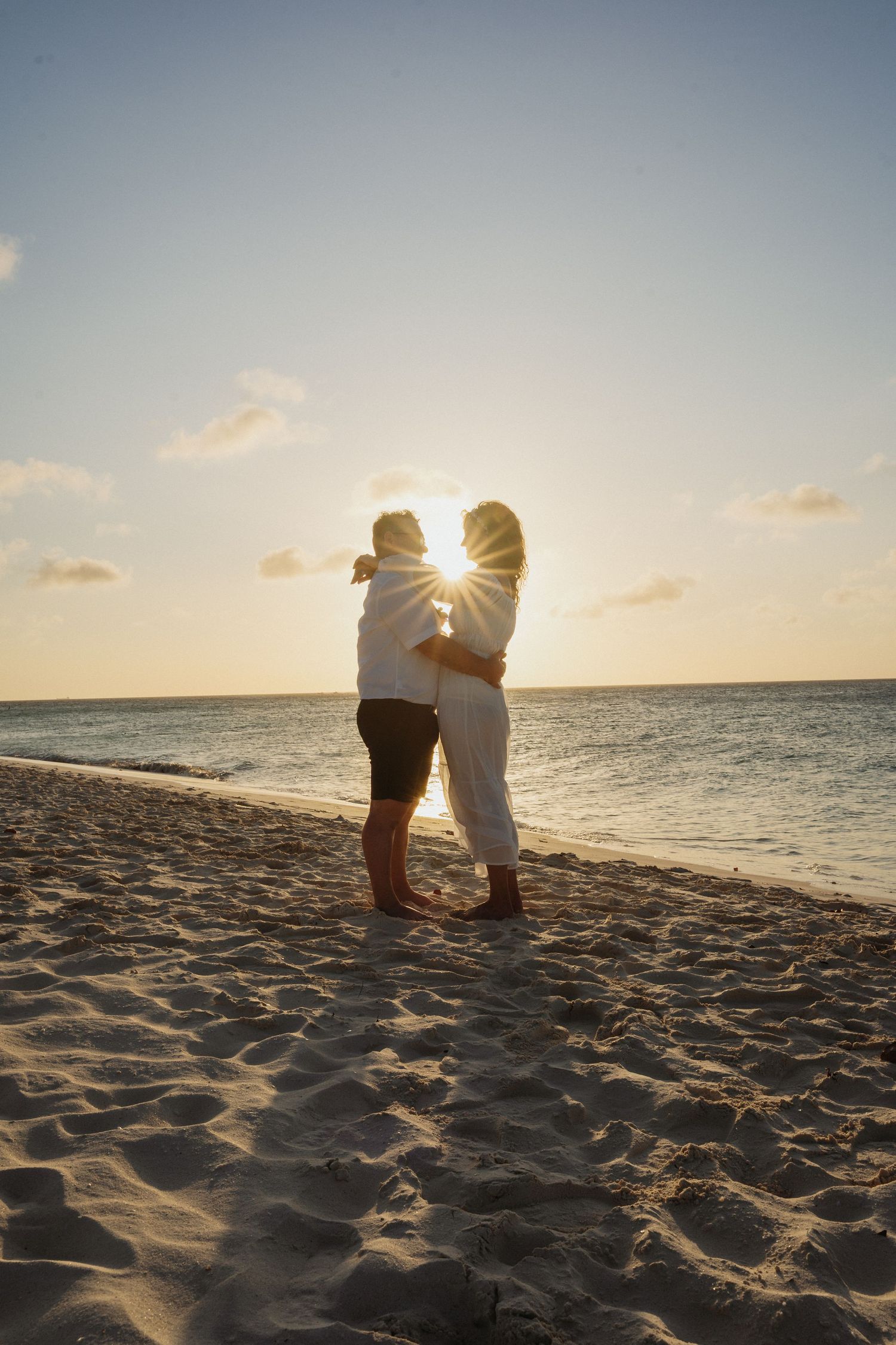 Silhouettes of a couple sitting together on a beach at sunset with the ocean horizon in view.