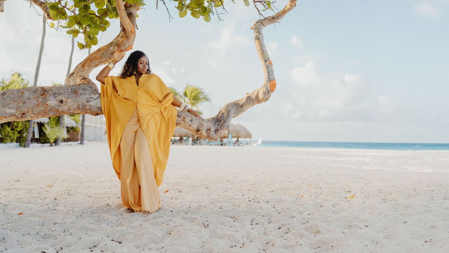 A person in a flowing yellow dress walks gracefully along a pristine white sand beach with turquoise ocean waters.