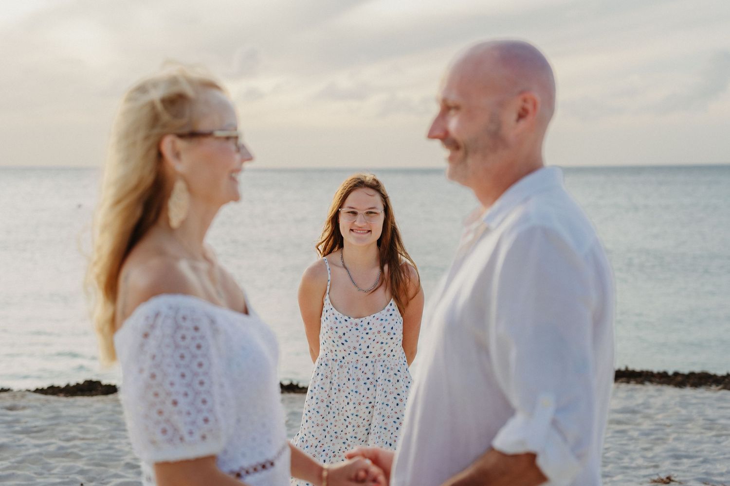A romantic beach wedding ceremony takes place at sunset with the ocean and rock formations in the background.
