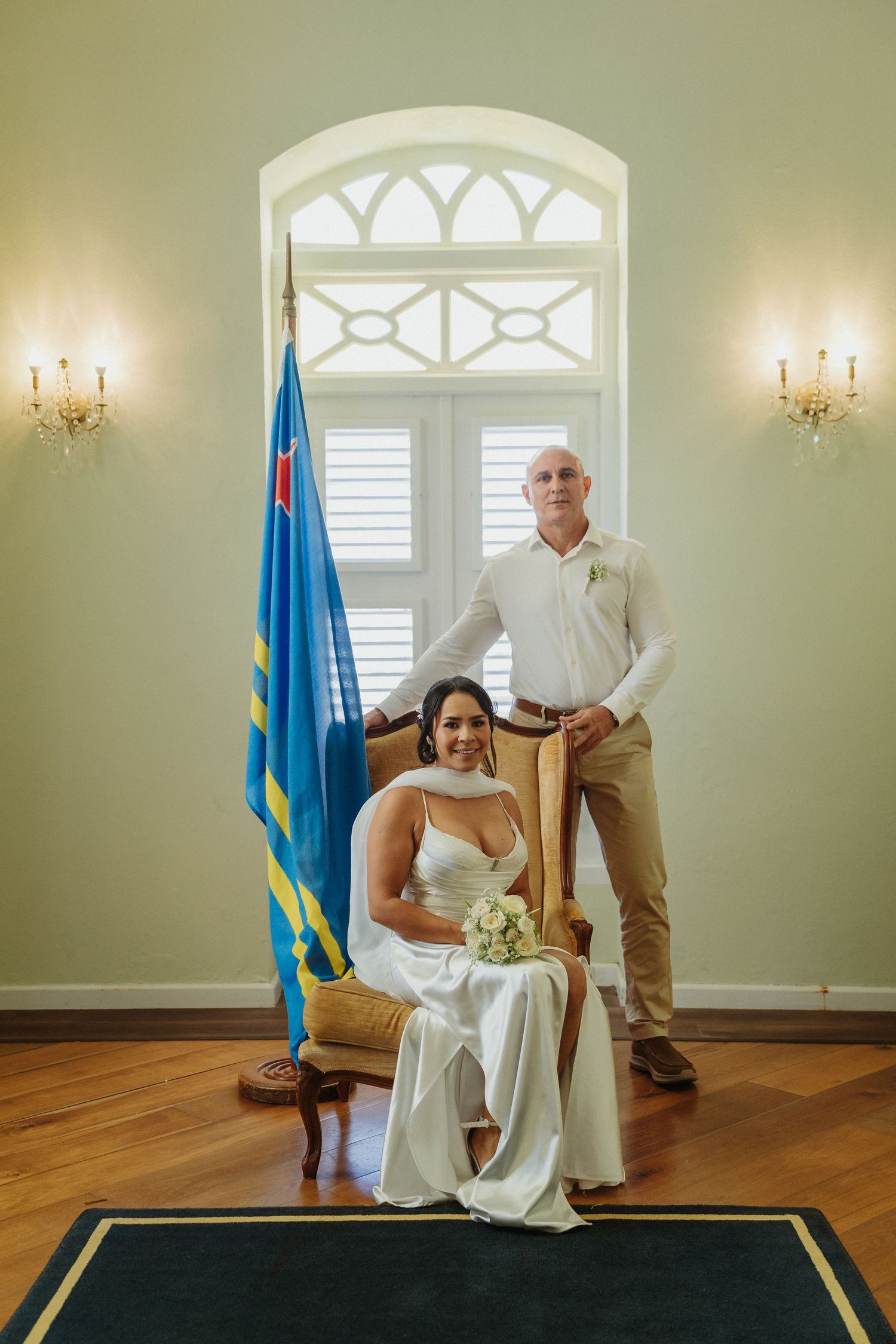 Intimate ceremony setup in a bright room with hardwood floors, green walls and decorative arched windows.