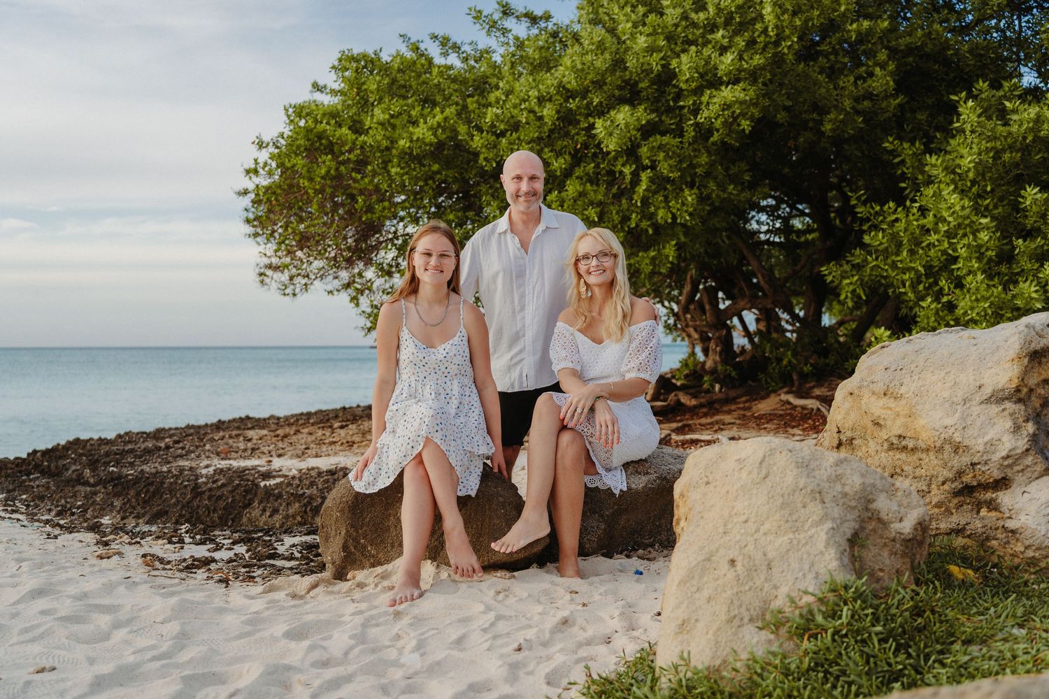 Family group enjoying a casual photo session together on a tropical beach with lush greenery and ocean views.