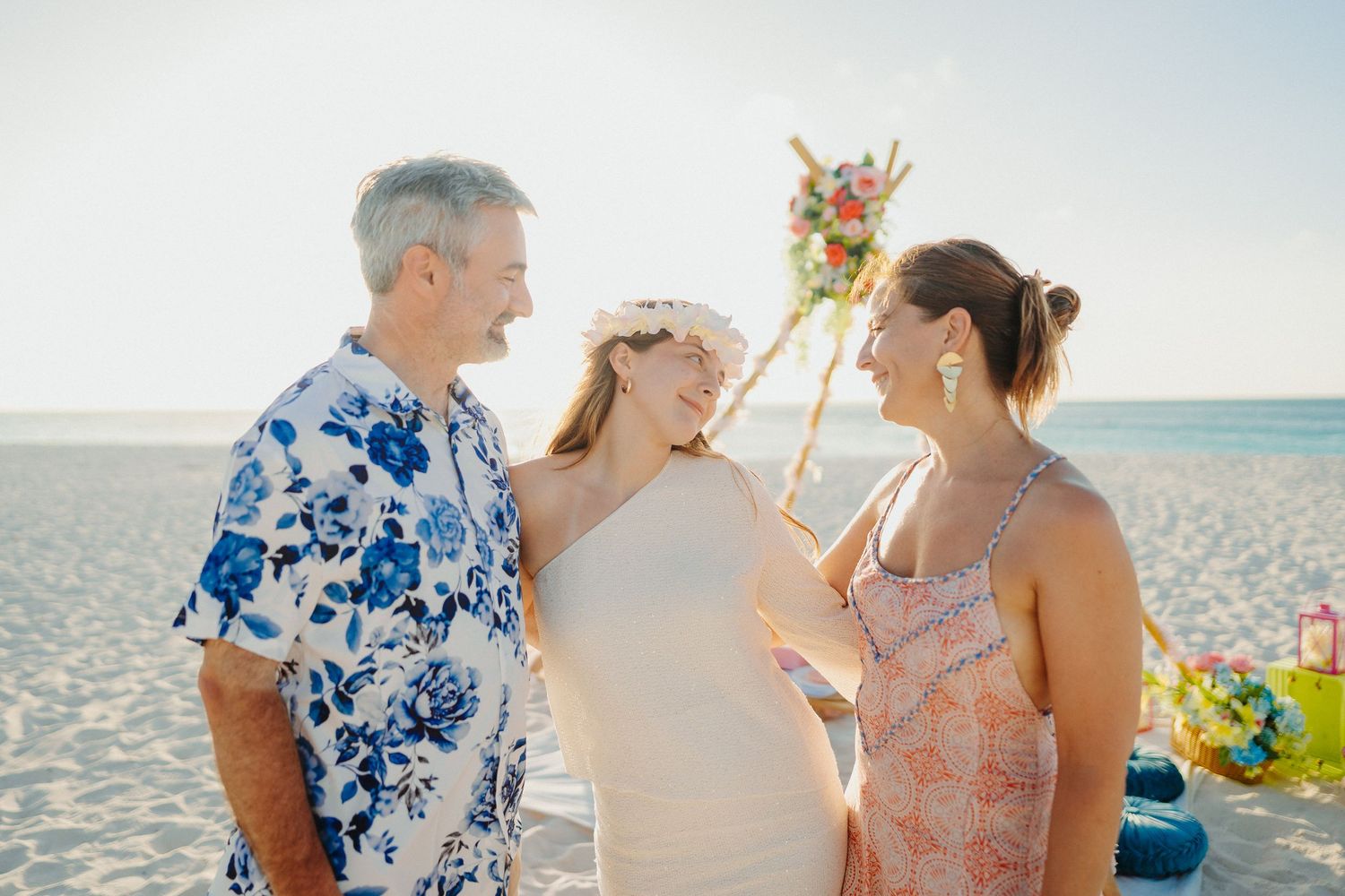 A couple in floral attire shares romantic moments on a sunny beach during a tropical wedding photo session.