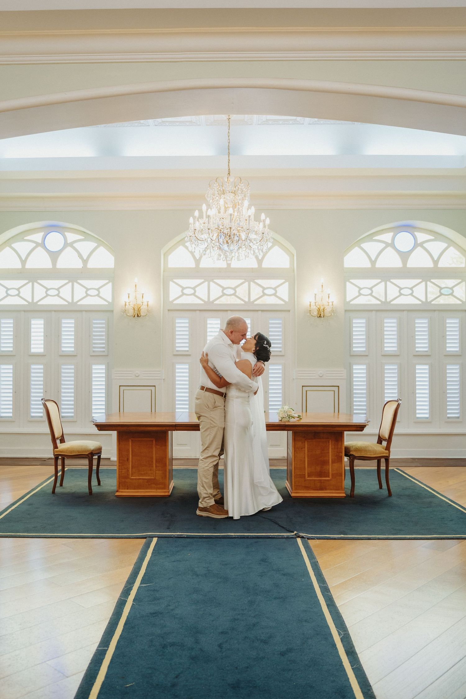 Elegant ballroom interior with teal carpet, white walls, crystal chandeliers and arched windows creates a romantic atmosphere.