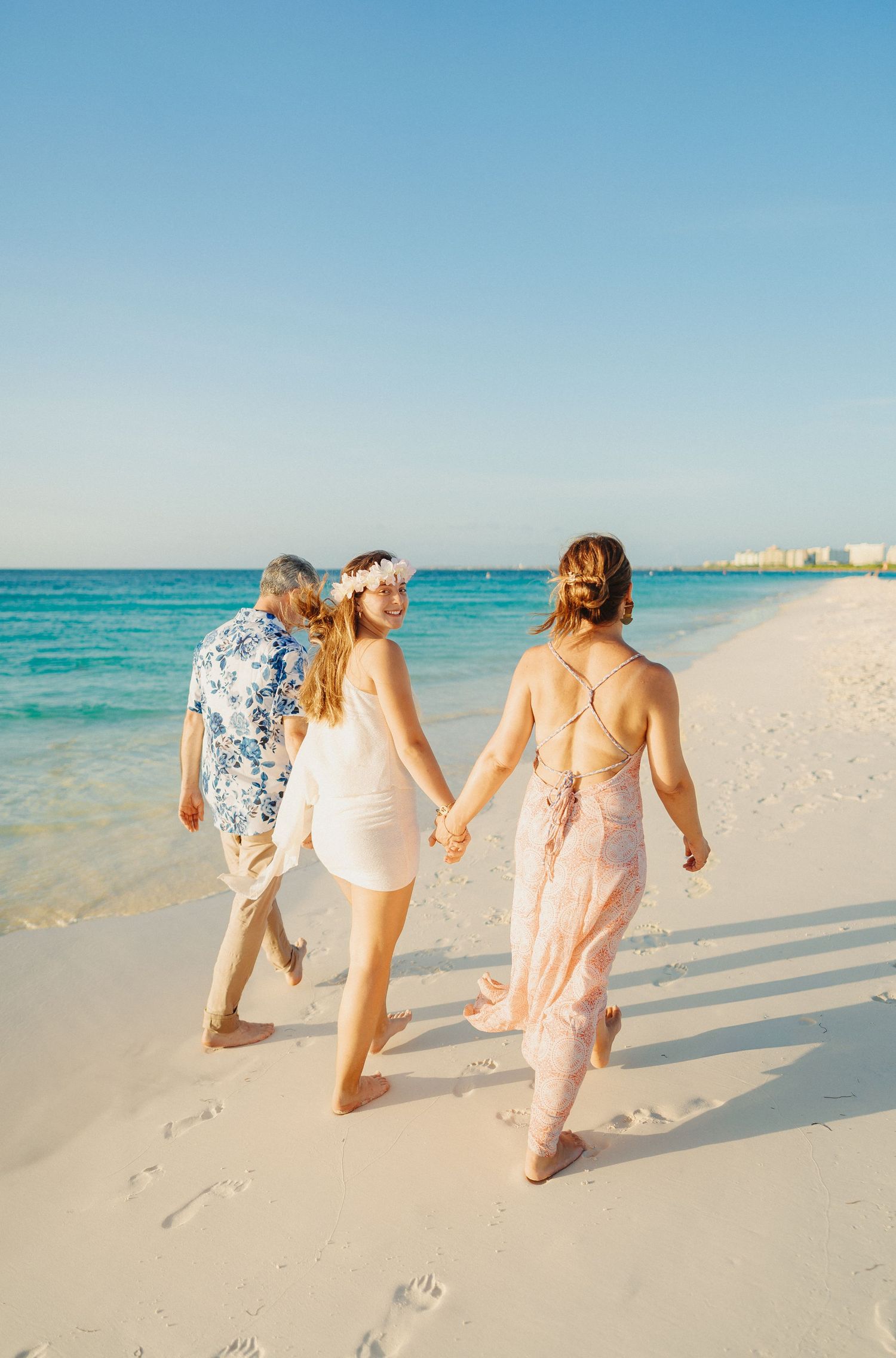 People walking together on a pristine white sand beach with turquoise ocean waters in the background.