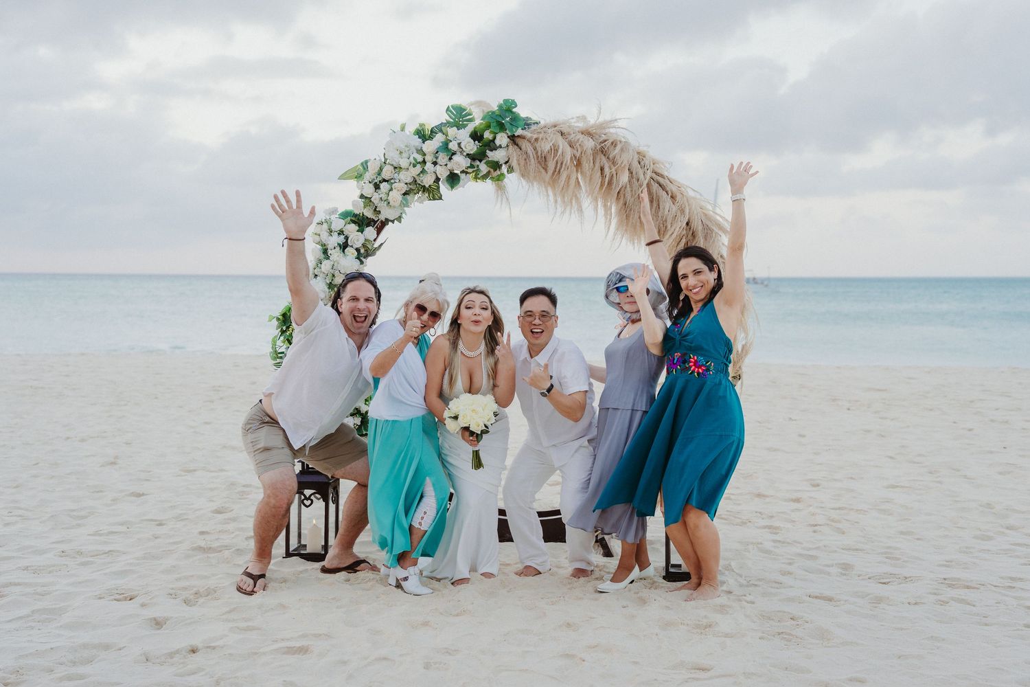 Wedding party celebrates on beach with tropical arch and turquoise ocean views.