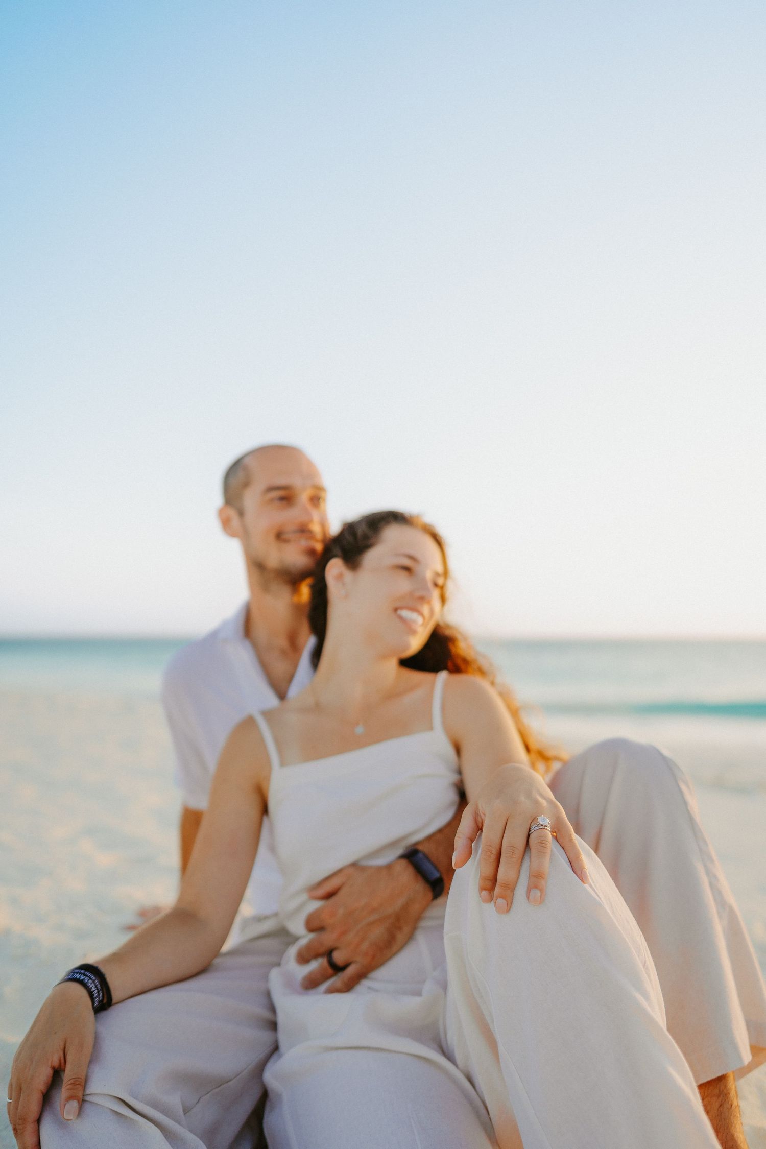 Couple lounging together on white sand beach during sunset.