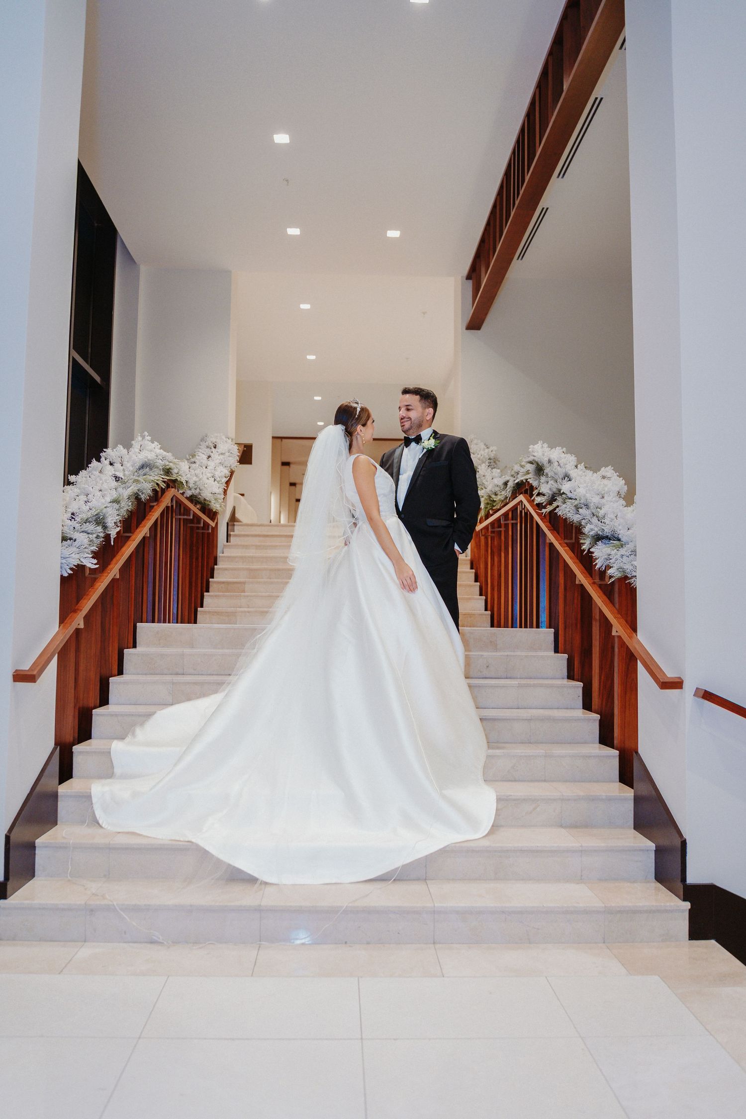 Multiple views of a bride's dramatic cathedral train trailing down marble stairs decorated with white floral arrangements.