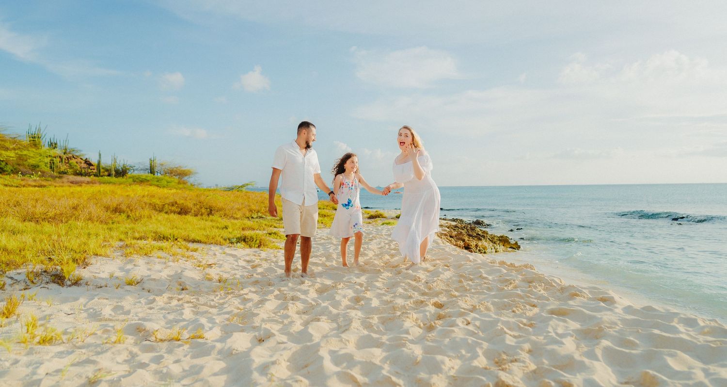 A family walks together along a scenic tropical beach with turquoise waters and golden sand during sunset.