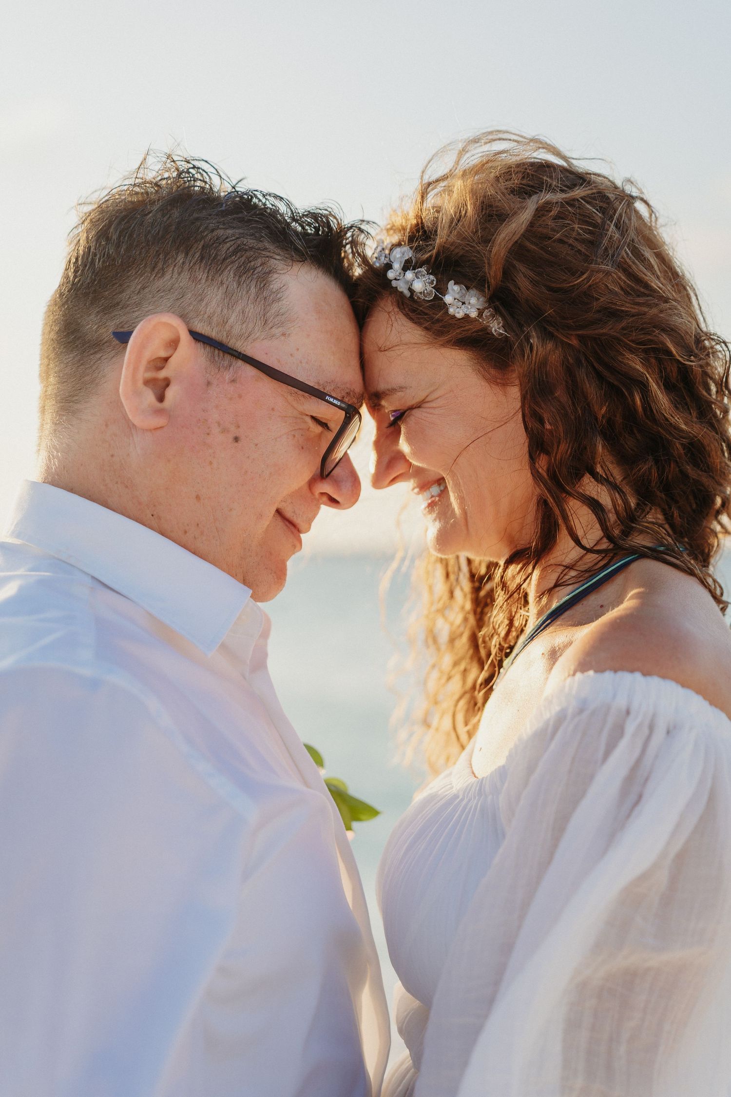 A romantic moment captured at sunset as a couple shares an intimate forehead touch on the beach.