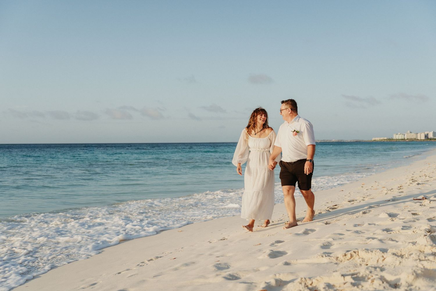 People walking along a pristine white sand beach with turquoise waters and clear blue skies.