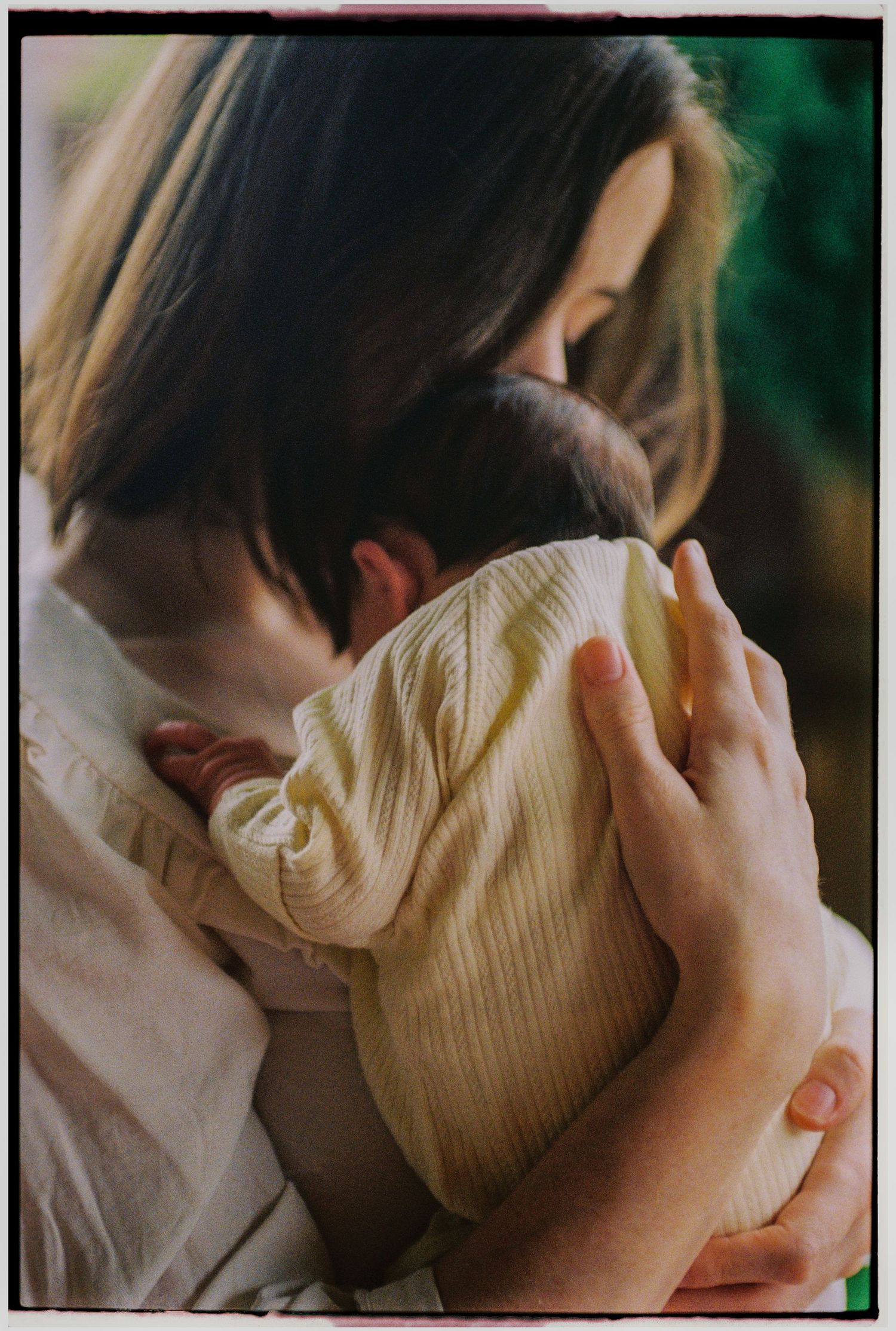 A mother tenderly holds her newborn baby dressed in a yellow ribbed outfit, cradling them close to her chest.