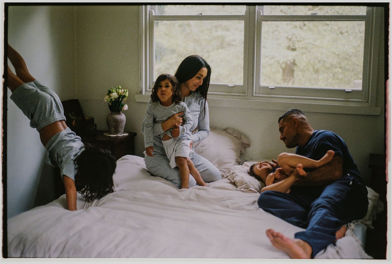 Family enjoying a playful morning together on a white bed, with children and parents laughing in a cozy bedroom.