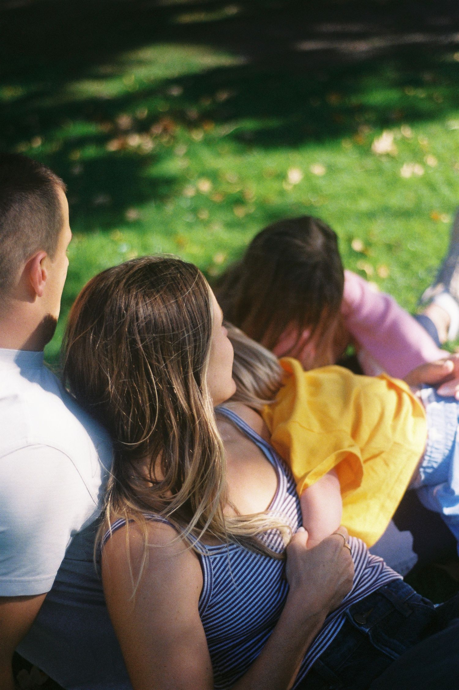 Family sitting together outdoors on a sunny day, relaxing on grass in a park setting.
