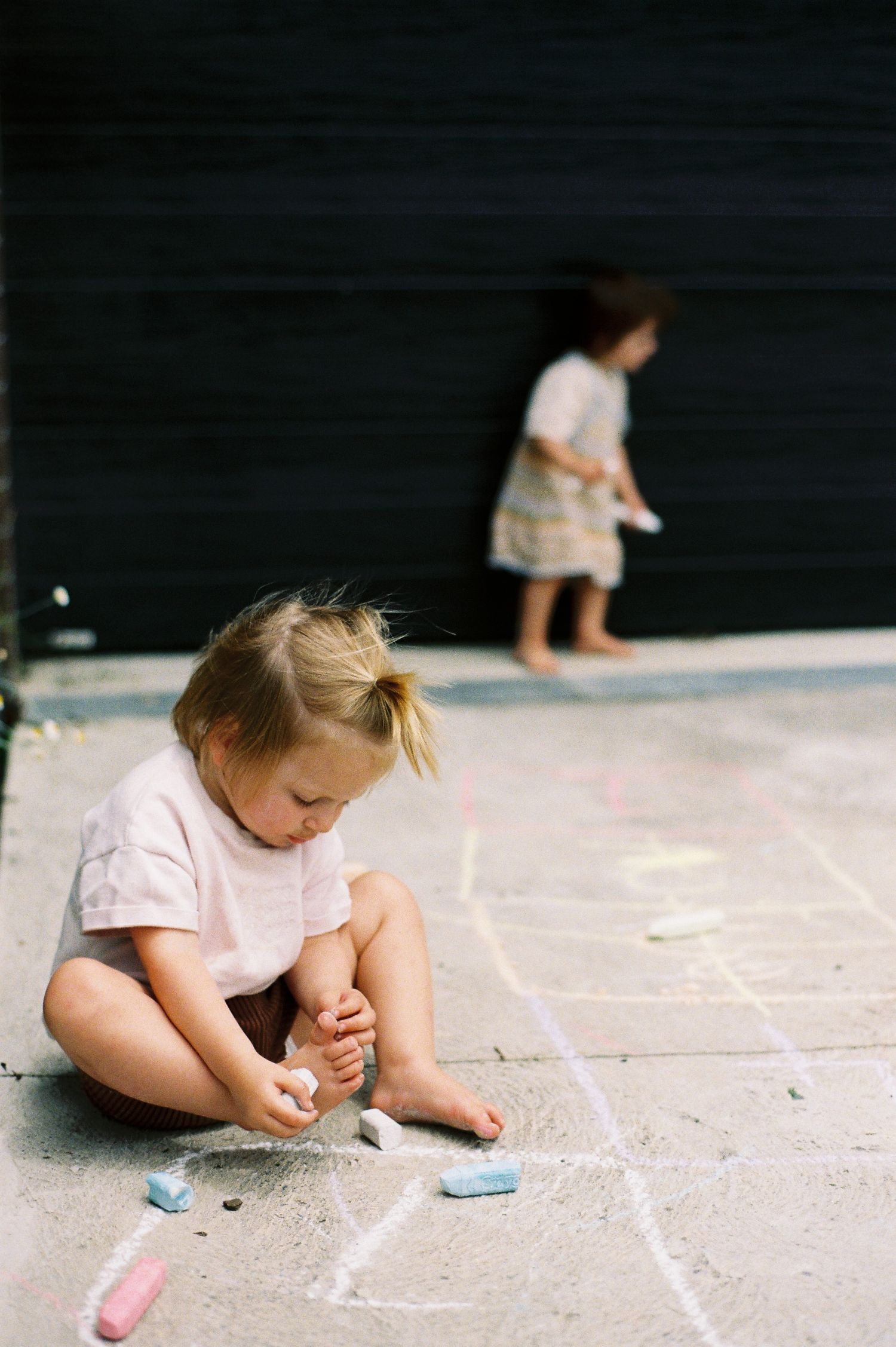 A child sits on concrete drawing with chalk in a sequence of progressive movement frames.