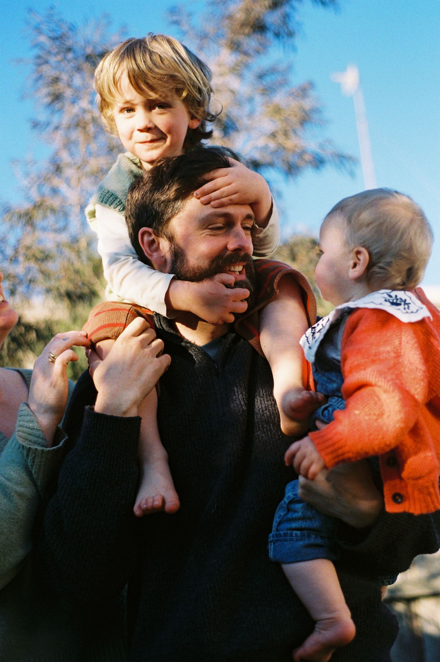 A sequence of four candid photos showing tender moments between a parent and baby against a sunny outdoor backdrop.