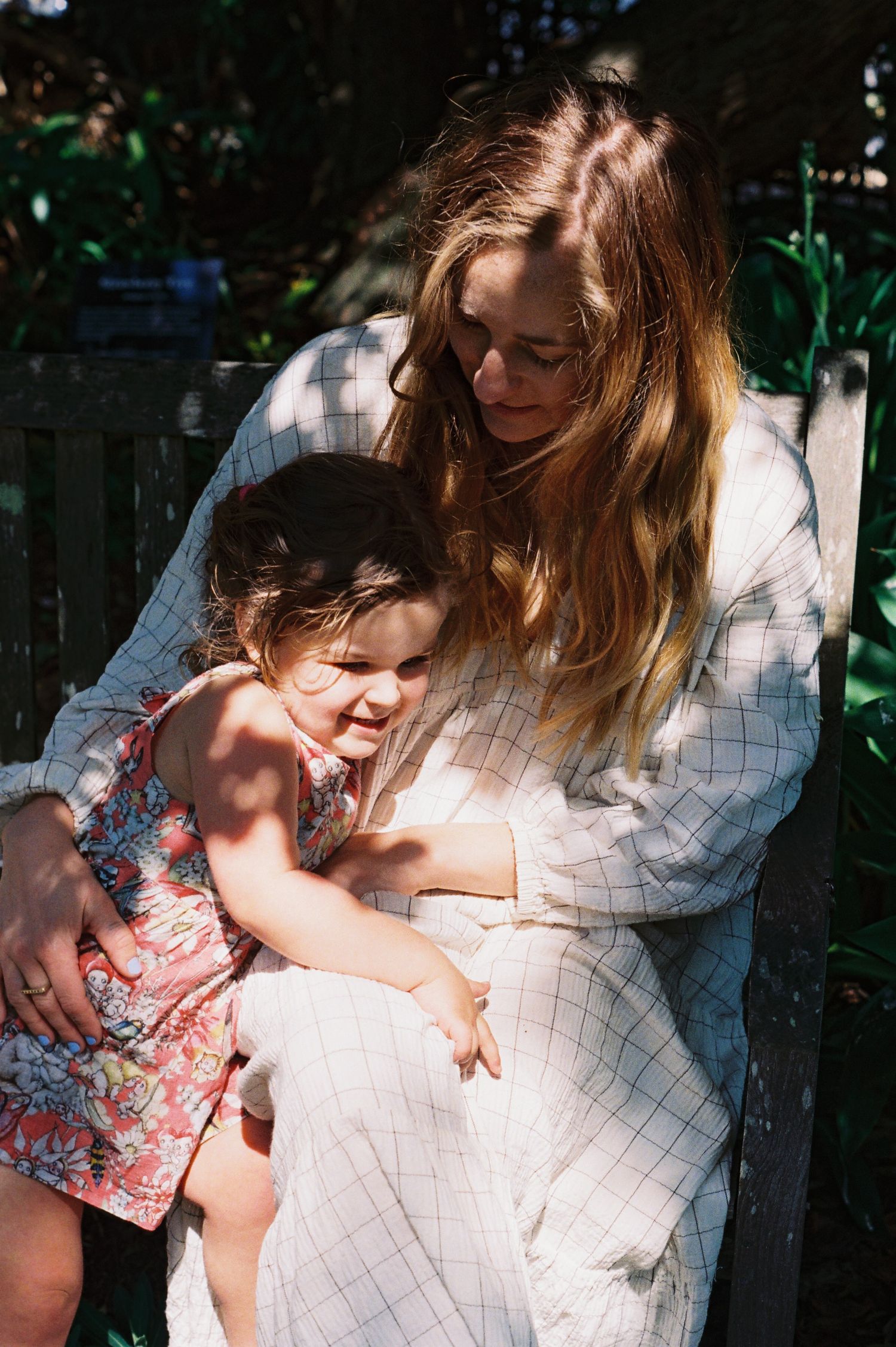 A tender moment captured in dappled sunlight as two people share an embrace in a garden setting.