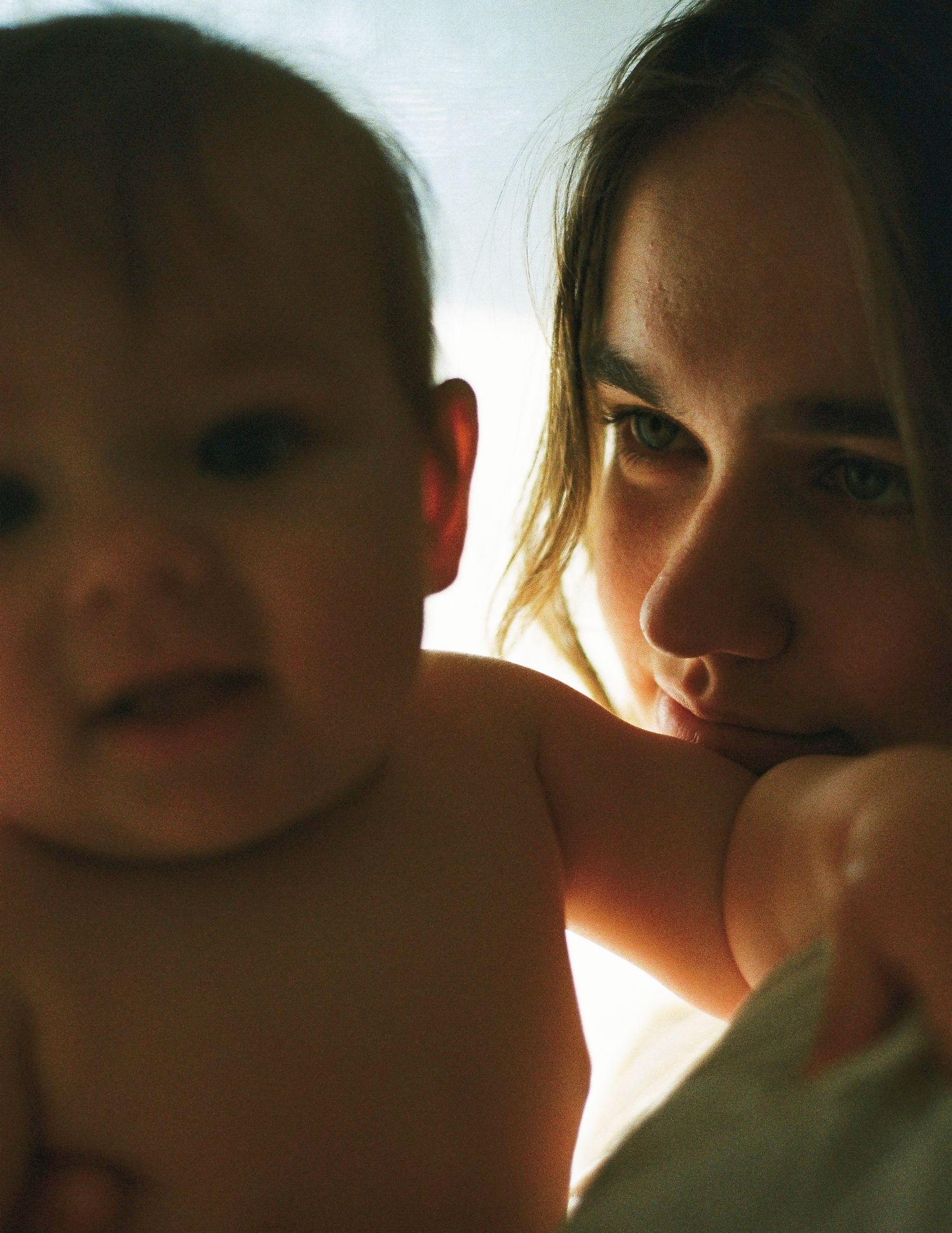 A young woman tenderly holds a baby, bathed in warm natural light in an intimate portrait.