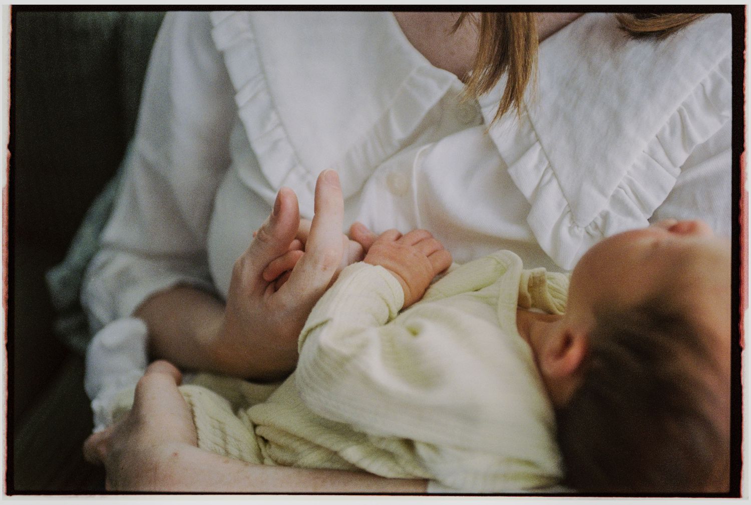 A mother in a white blouse tenderly holds her newborn baby dressed in a soft yellow outfit.