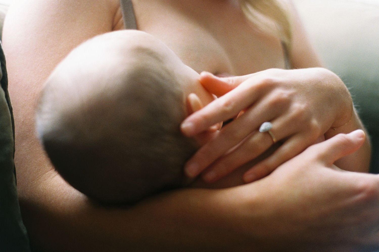 A tender moment of a baby breastfeeding while being cradled in loving arms with a wedding ring visible.