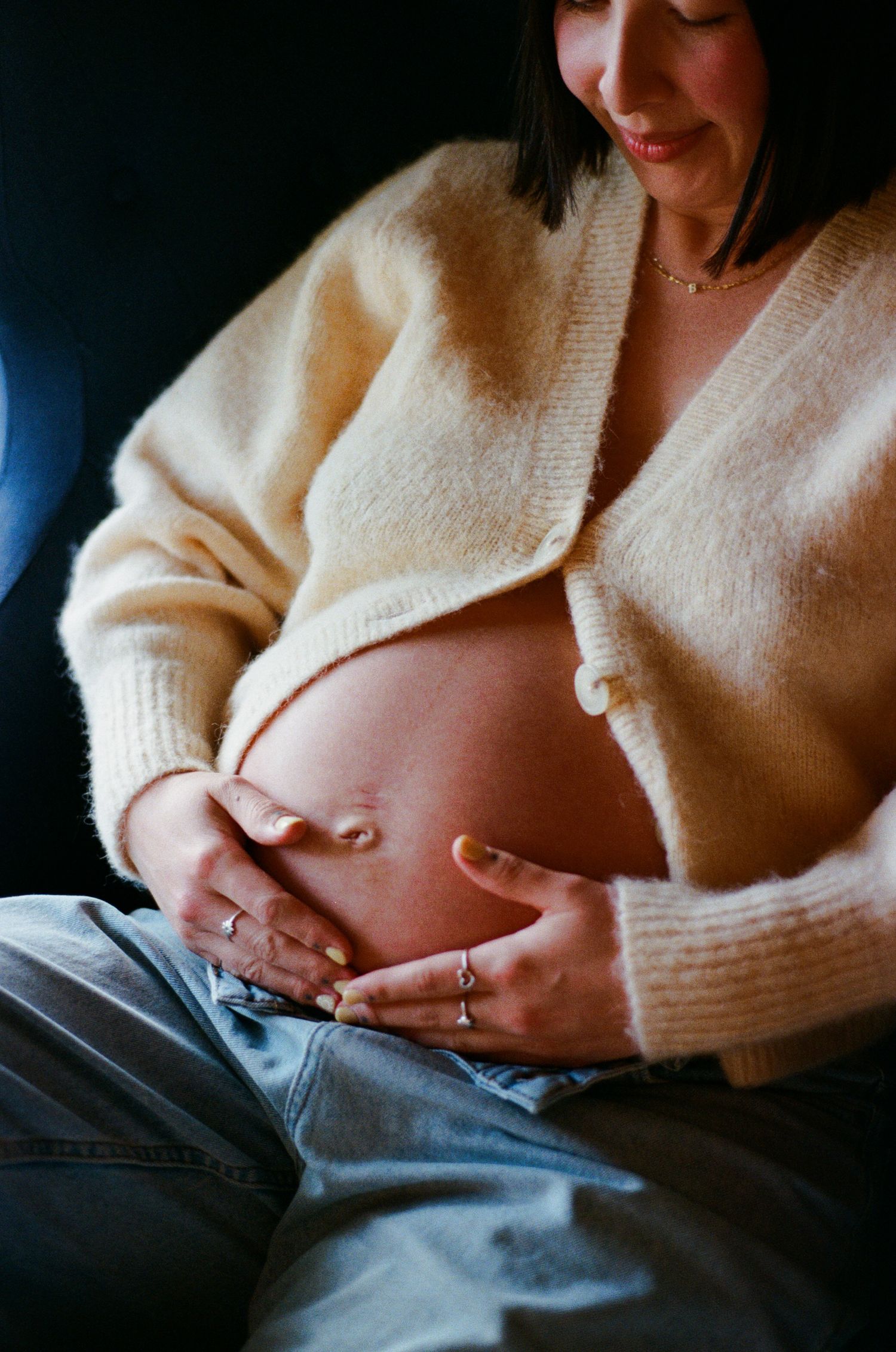 A pregnant belly being cradled by hands wearing in soft lighting. Mornington-Peninsula and Melbourne Film Photography