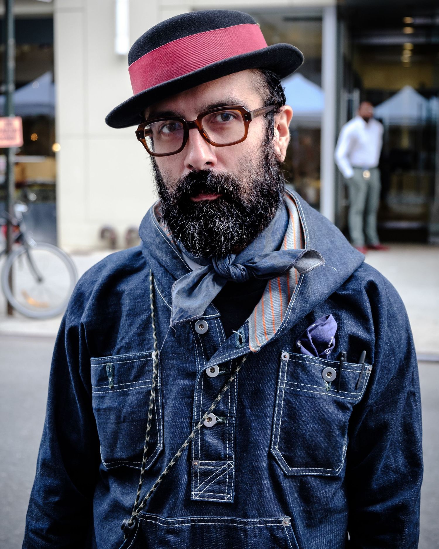 A person wearing glasses and a pink cap poses in a denim jacket against an urban background.