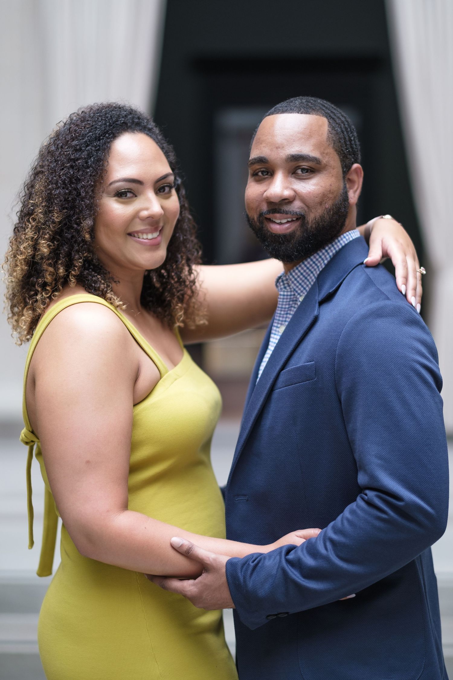 Happy couple in yellow dress and navy suit sharing playful moments during a photoshoot.
