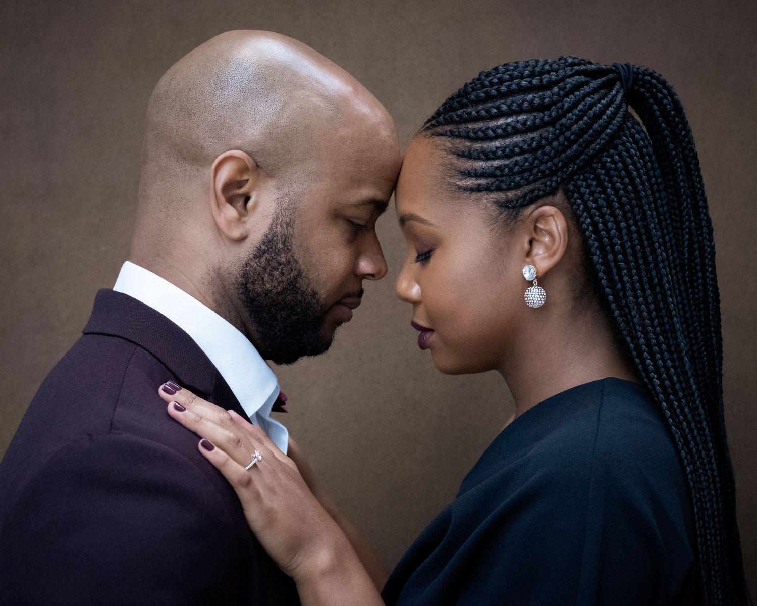Intimate portrait of a couple in formal attire sharing a tender moment against dark background.