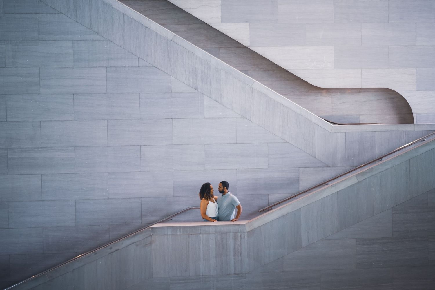 Couple walking along a modern concrete hallway with dramatic angular architecture.
