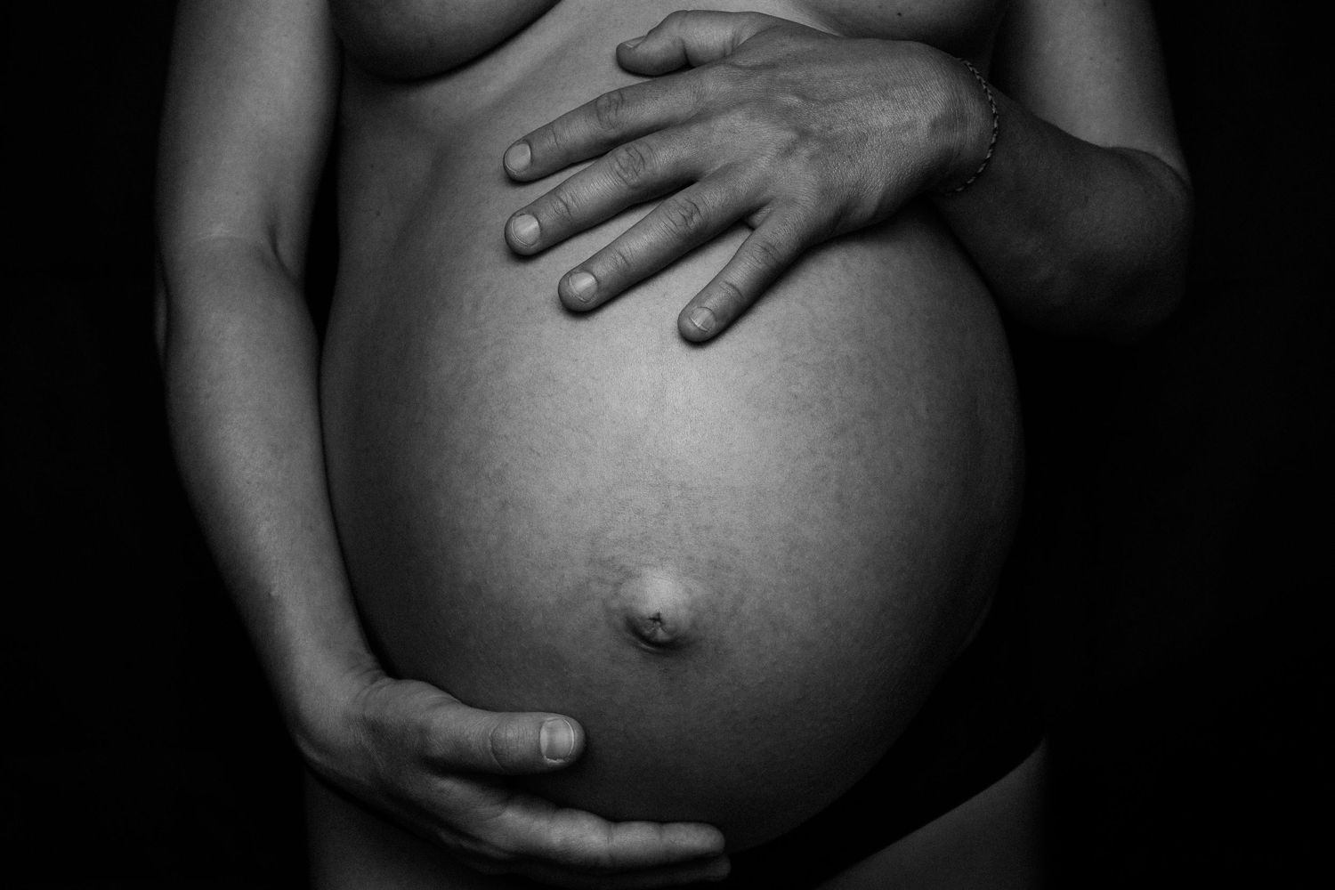 Black and white artistic photo of a pregnant belly with hands tenderly cradling the baby bump.