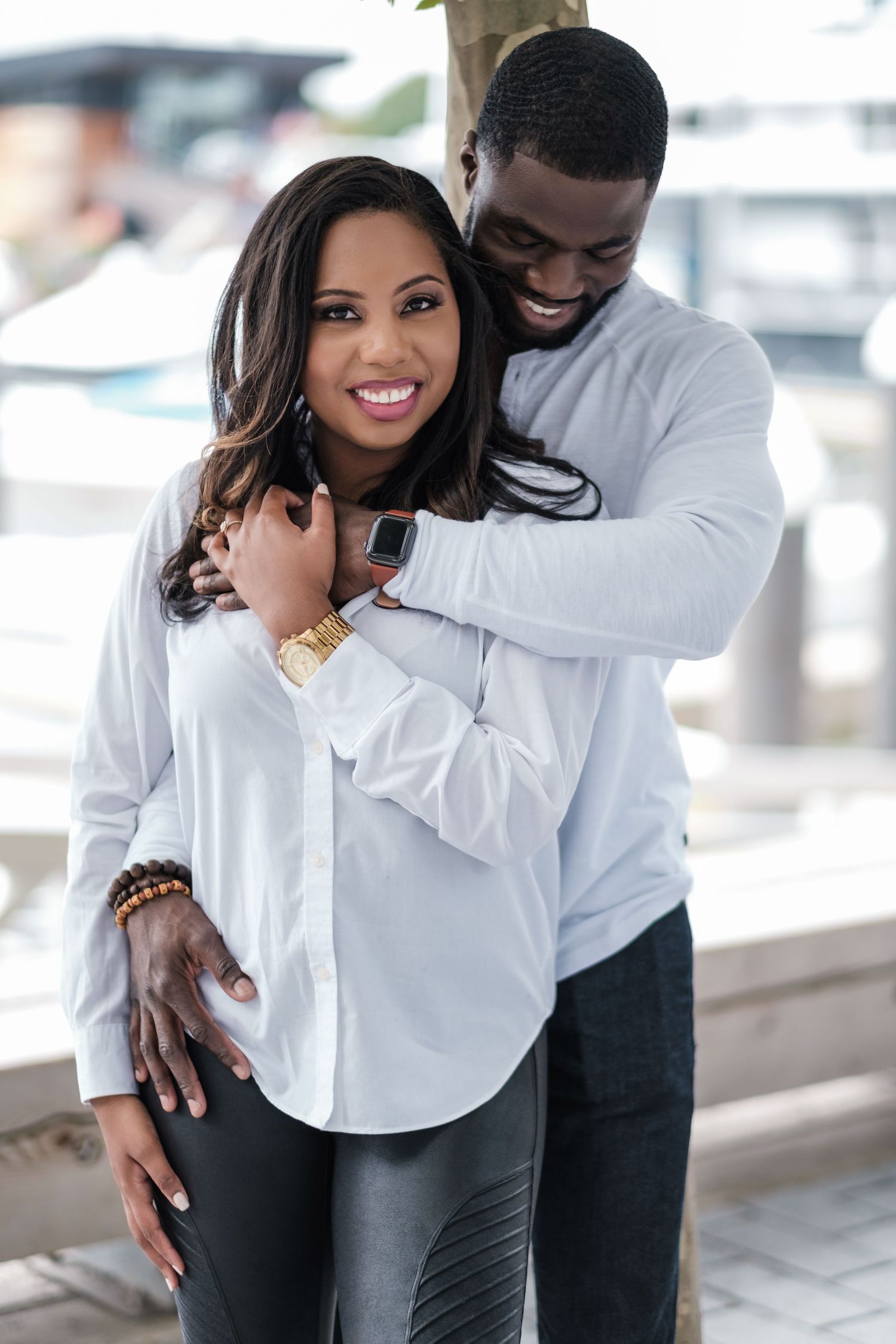 A romantic couple embraces while wearing matching white tops against a bright background.