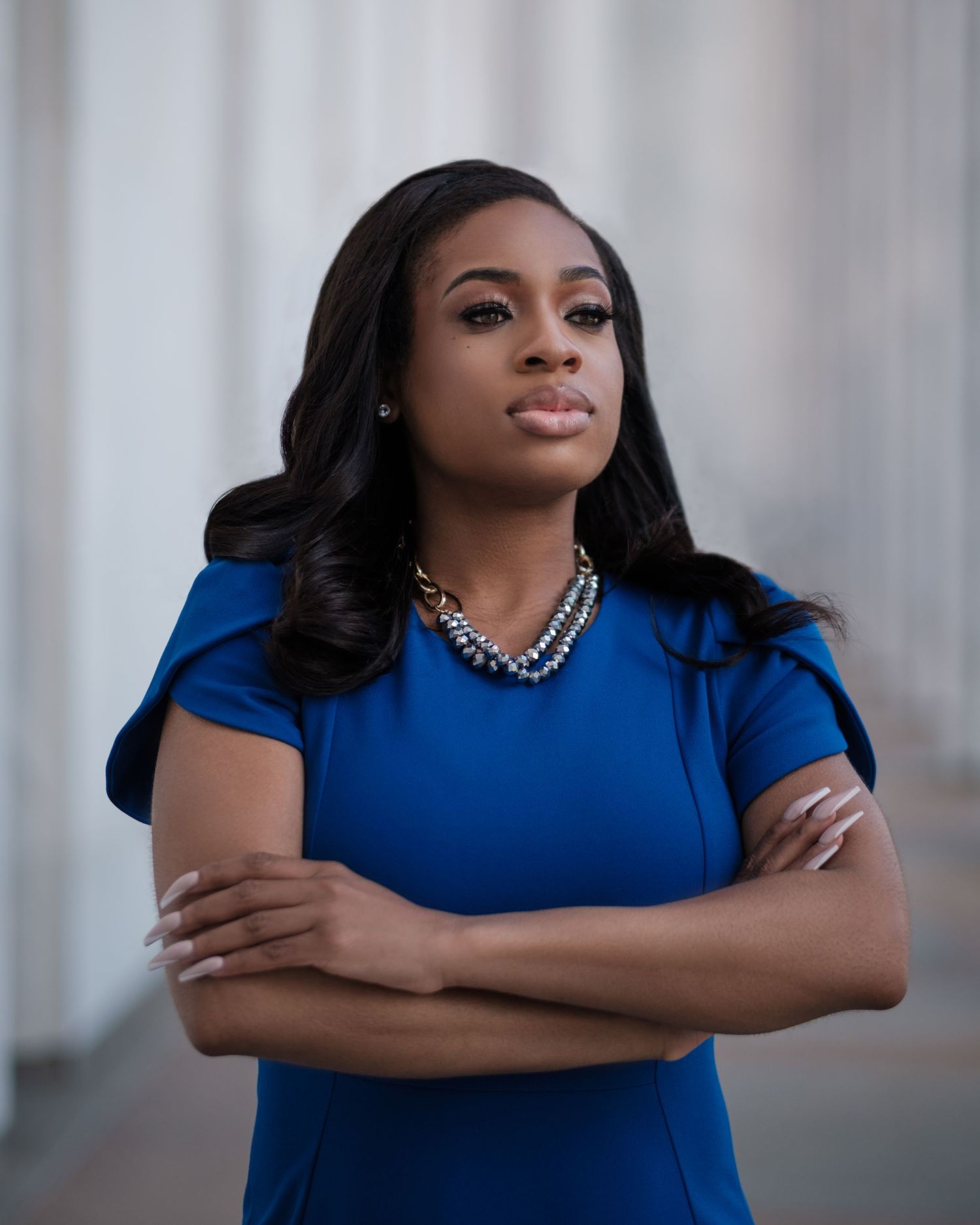 A woman in a royal blue dress poses confidently against a light background in a professional photoshoot series.