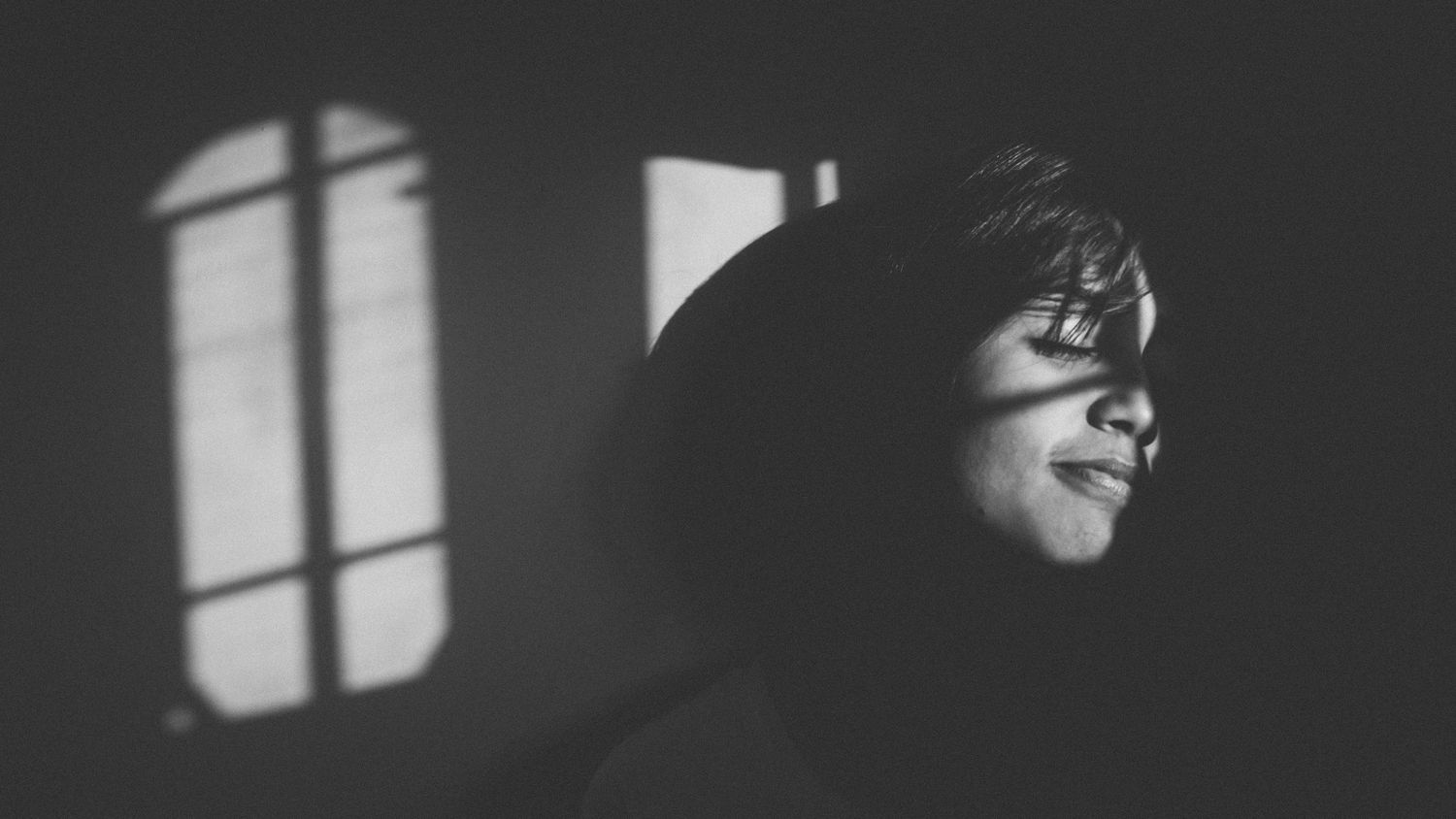 A dramatic black and white portrait showing shadows and window light.