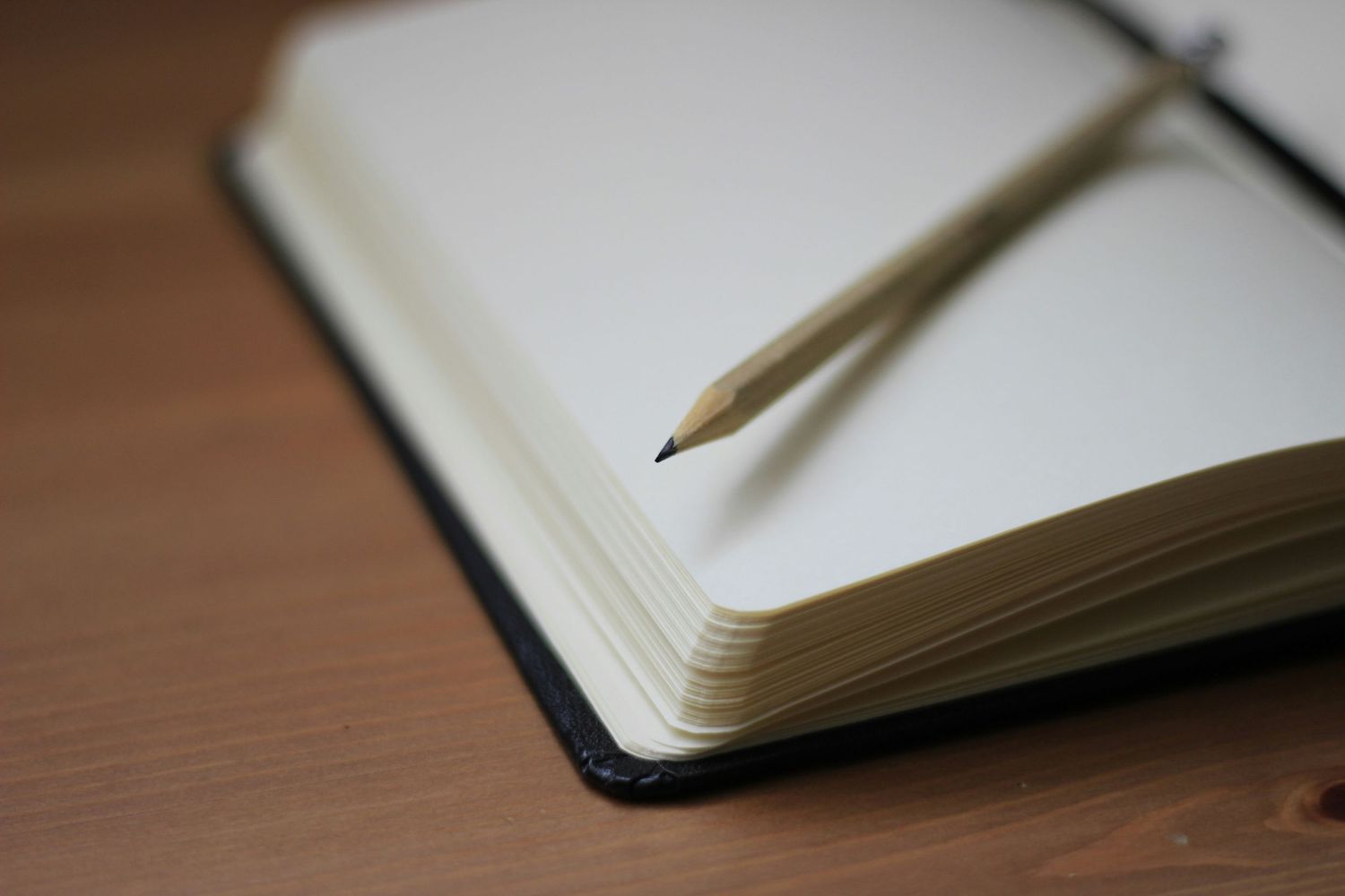 Open notebook with pencil on wooden desk in natural lighting.