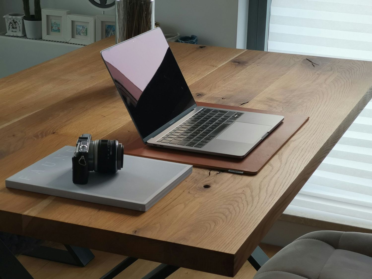 A wooden desk workspace with a laptop, camera, and minimal setup in natural light.